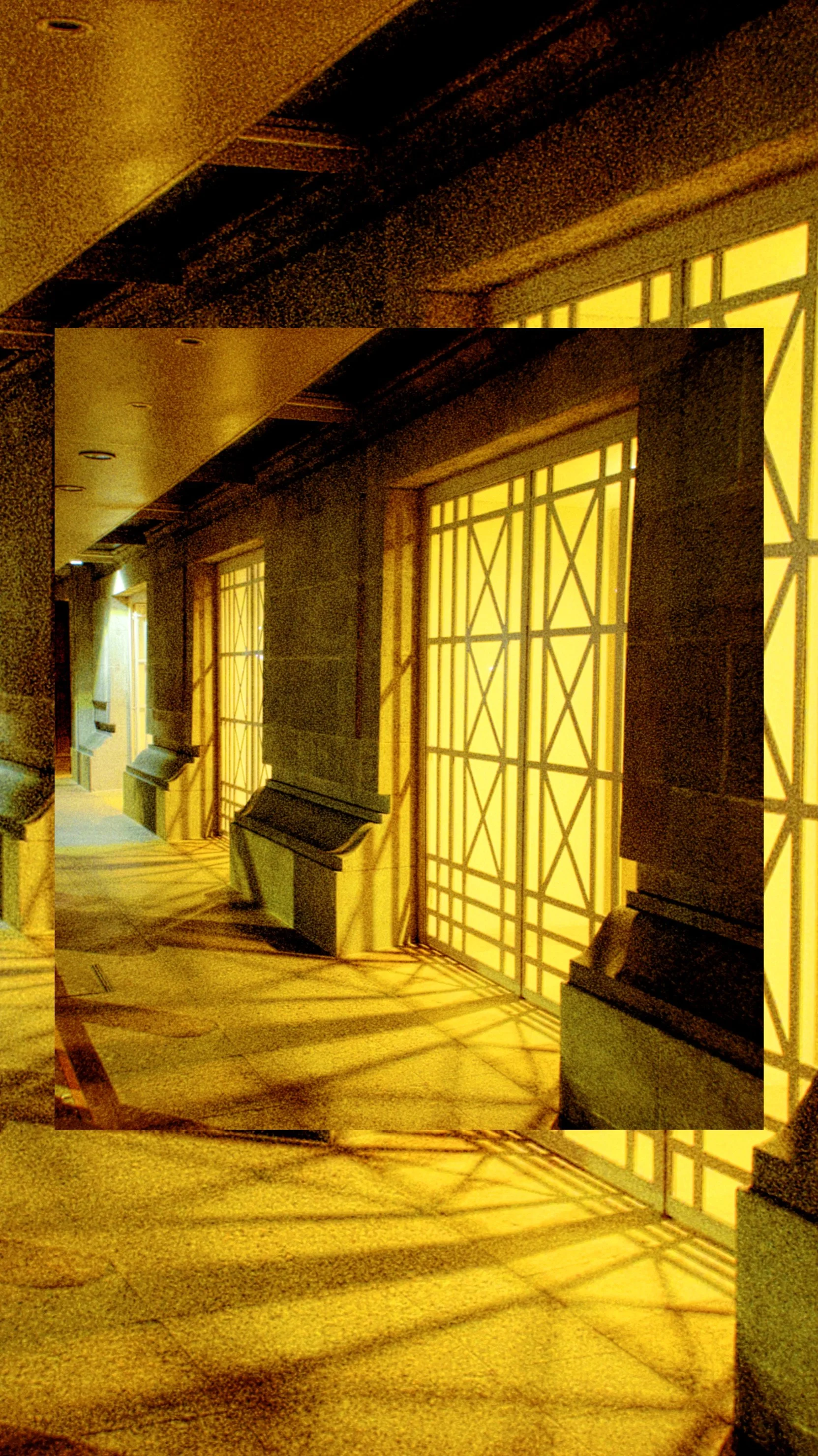 Indoor corridor with ornate lattice panels casting geometric shadows on the wall and floor, warm yellow lighting