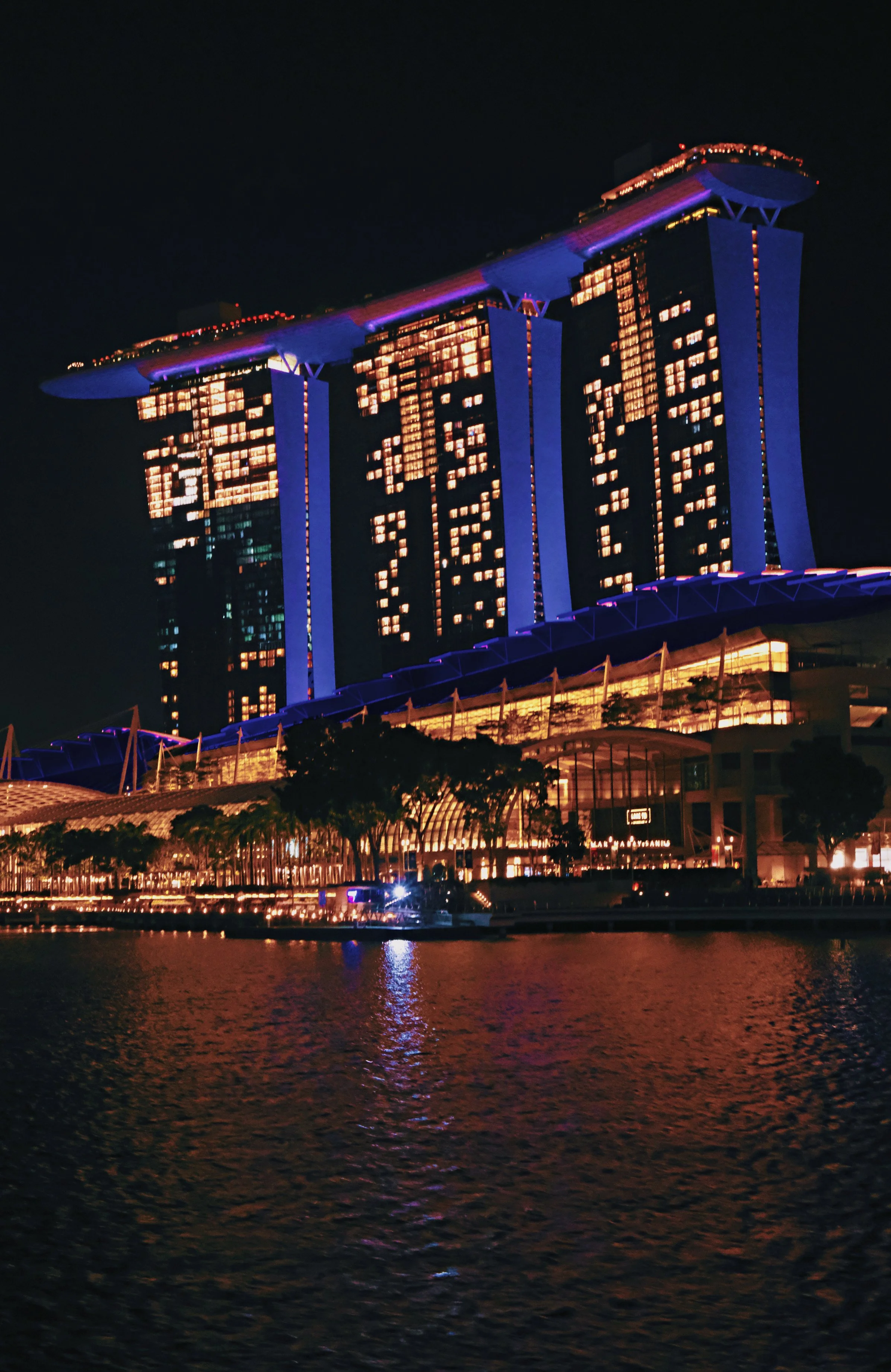 Night view of Marina Bay Sands hotel in Singapore illuminated with colorful lights, reflecting on the water.