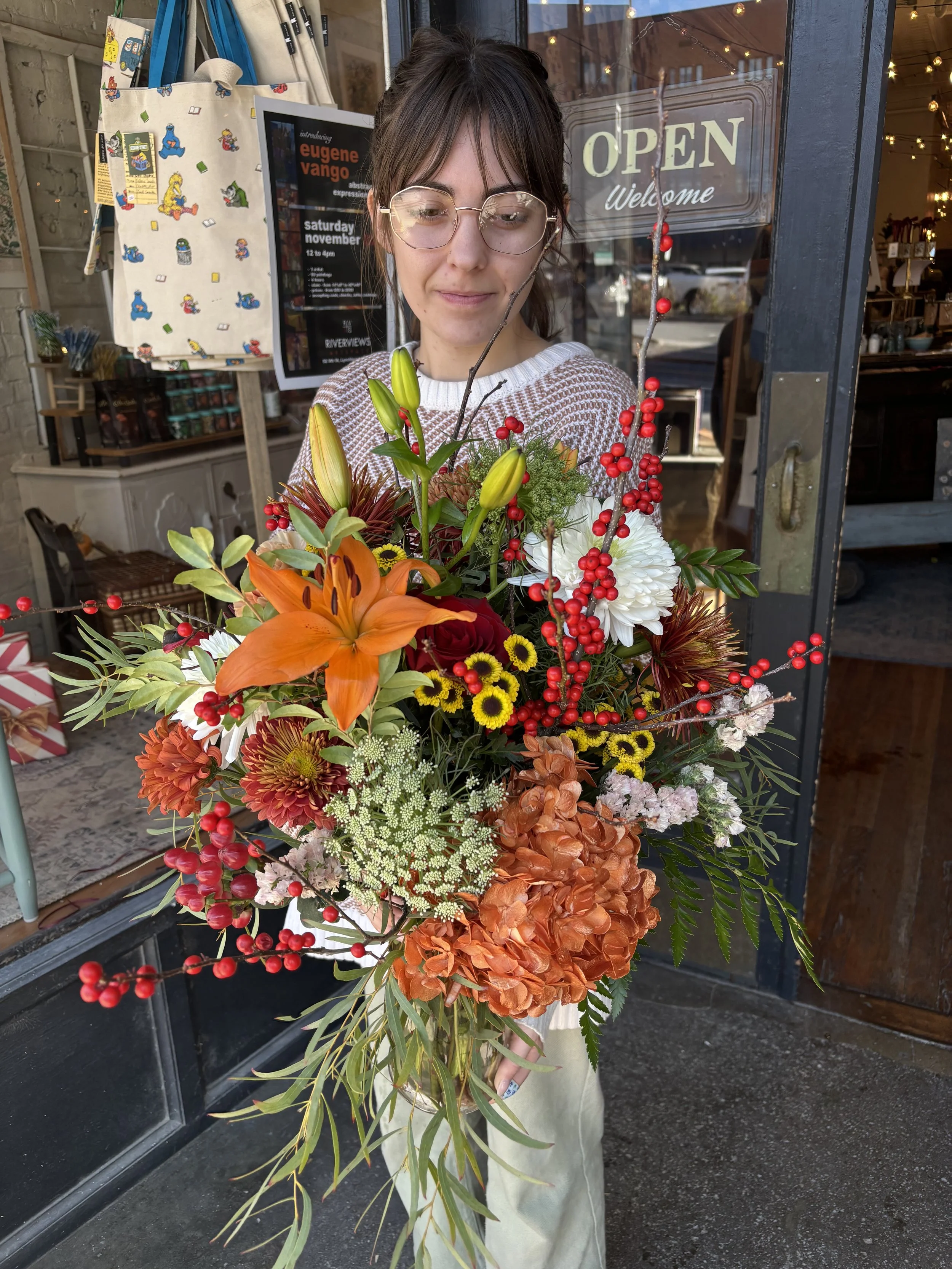 Young woman with glasses holding a large colorful flower bouquet outside of Lexie and Lee & Wild Grove Florals in Downtown Lynchburg VA