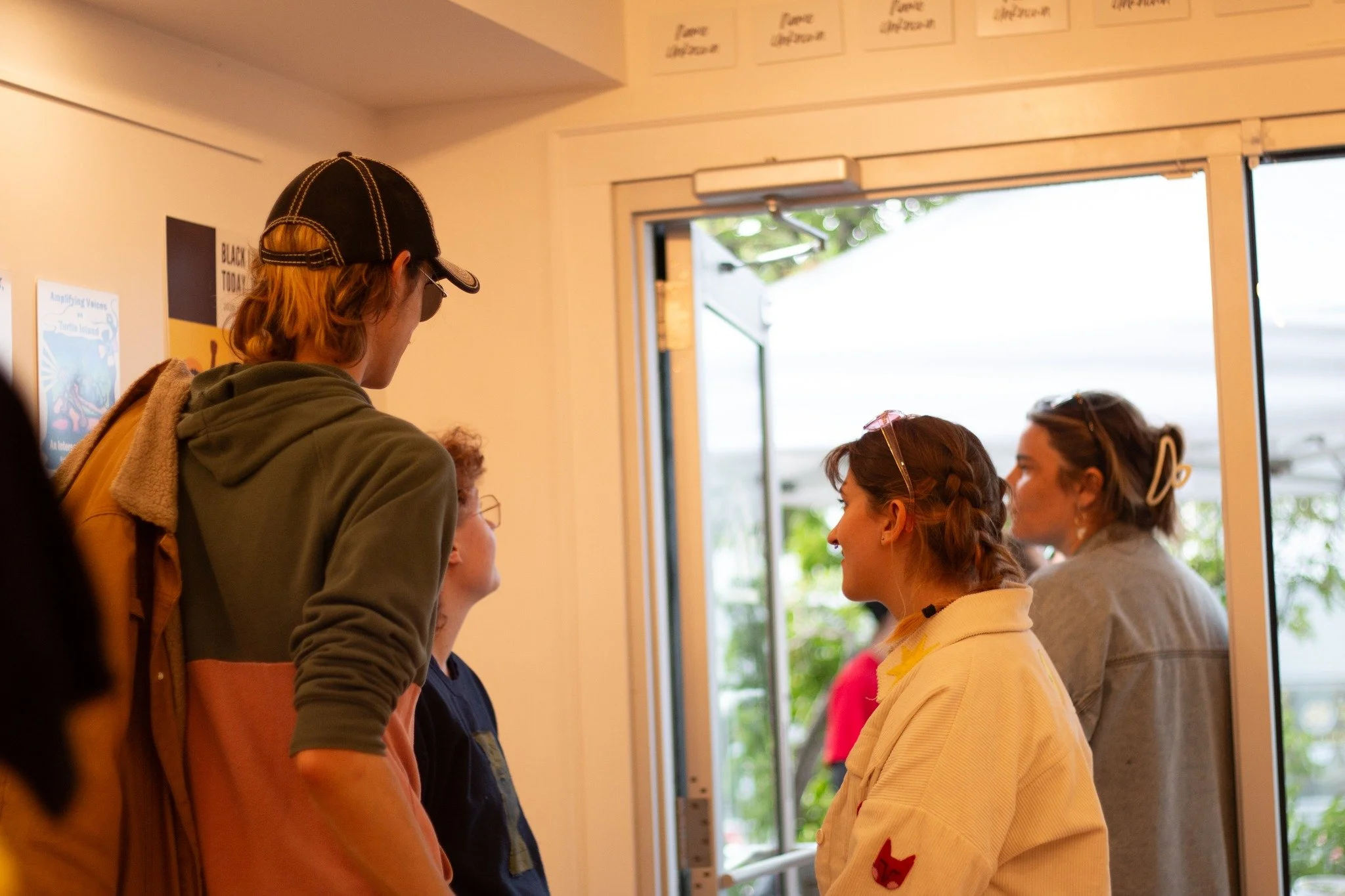 Group of young people inside a building near an open door, engaged in conversation, with some outside.