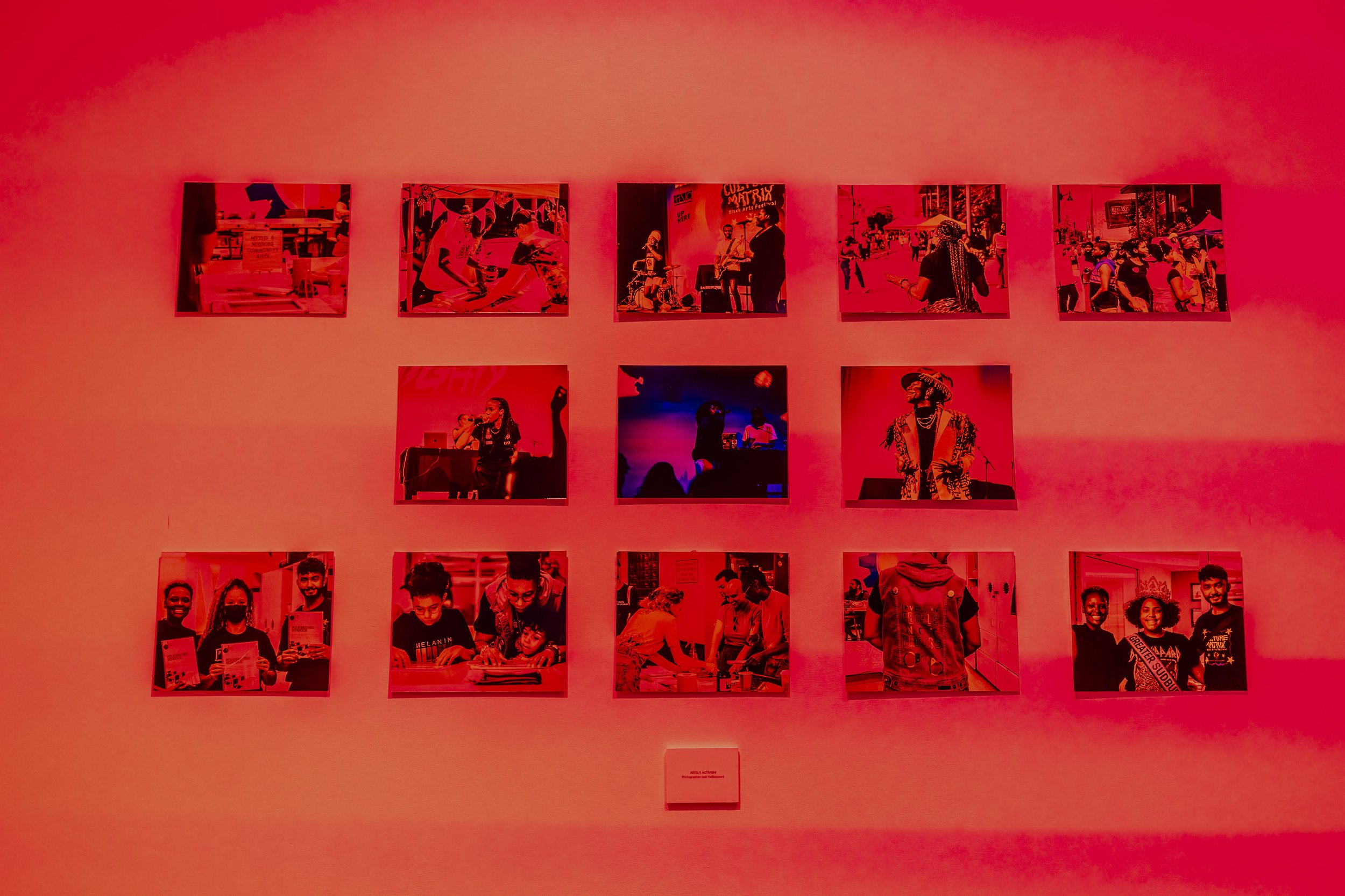 A wall displaying 15 photographs arranged in a grid of 3 rows and 5 columns, illuminated by red lighting.