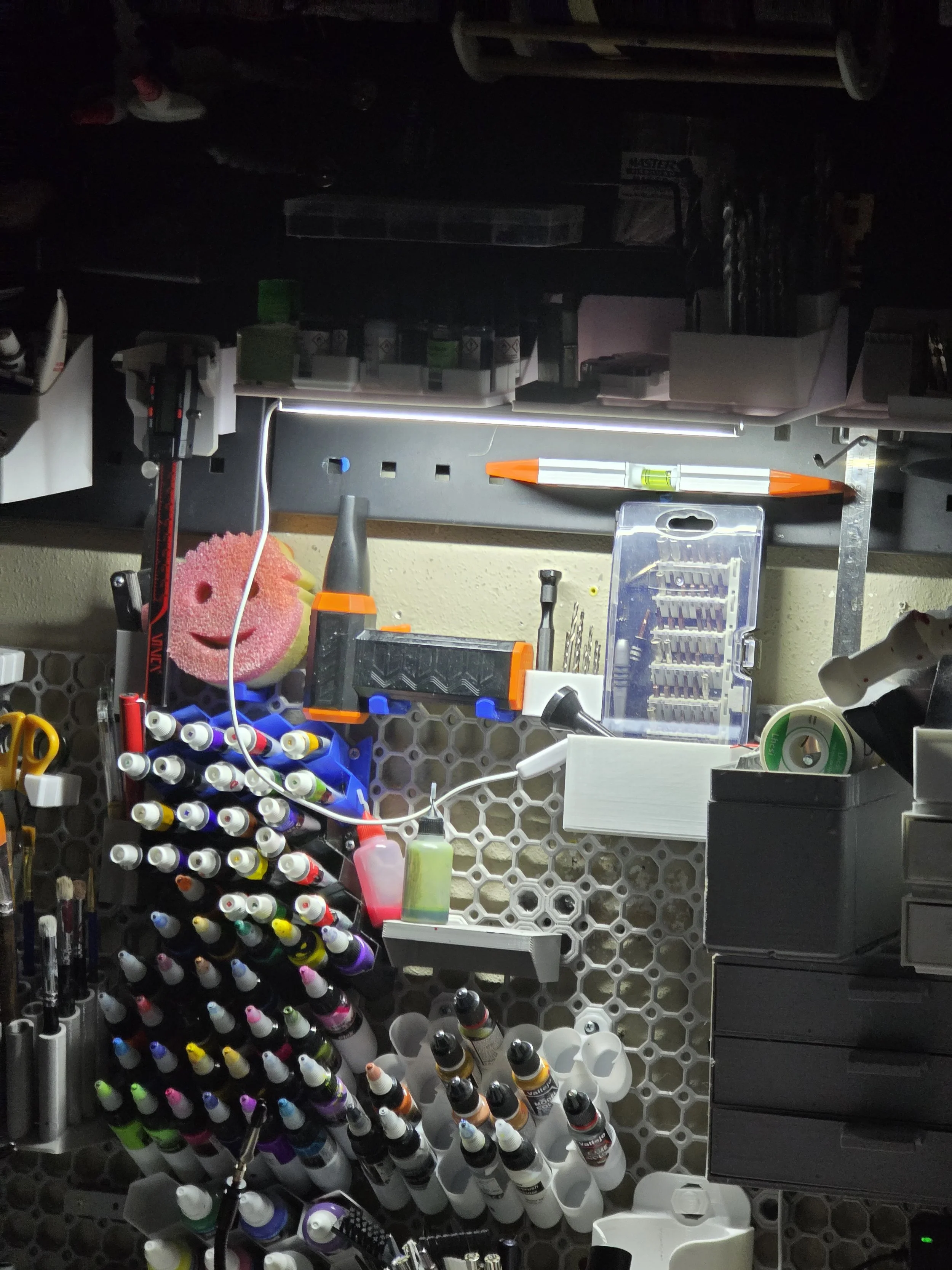 Tool and supply organization on a workshop wall, including bottle markers, a mini drill, screwdrivers, a pen, tape, and various small containers.