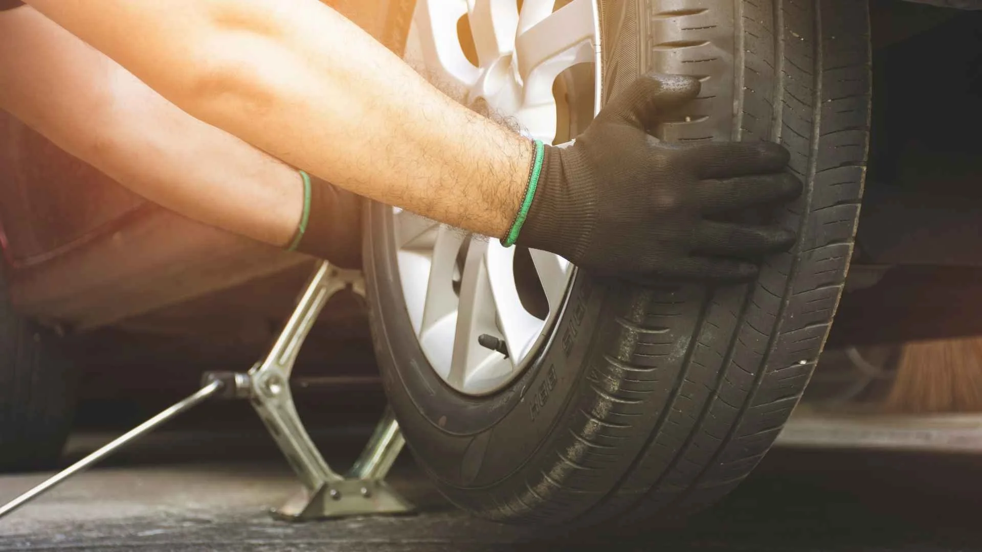 Person wearing black gloves changing a tire on a car with a metal highway jack.