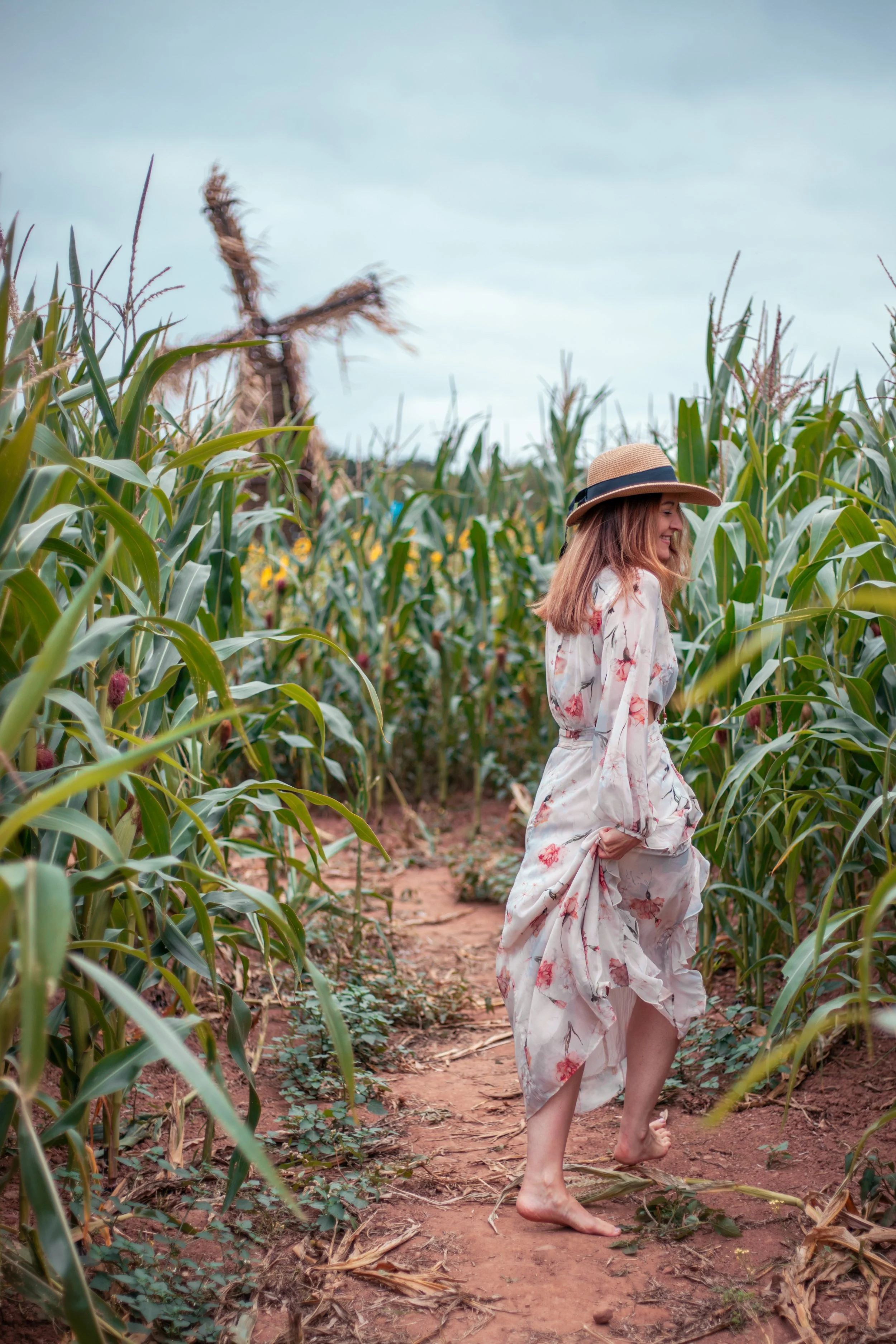 A woman in a floral dress and wide-brimmed hat walking barefoot through a cornfield. Natural beautiful portrait.