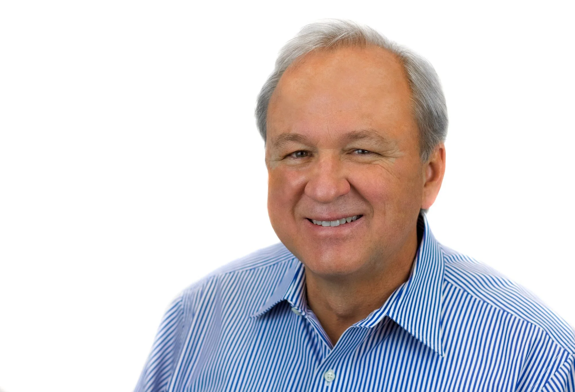 A smiling middle-aged man with light skin, gray hair, and wearing a blue and white striped dress shirt against a white background.