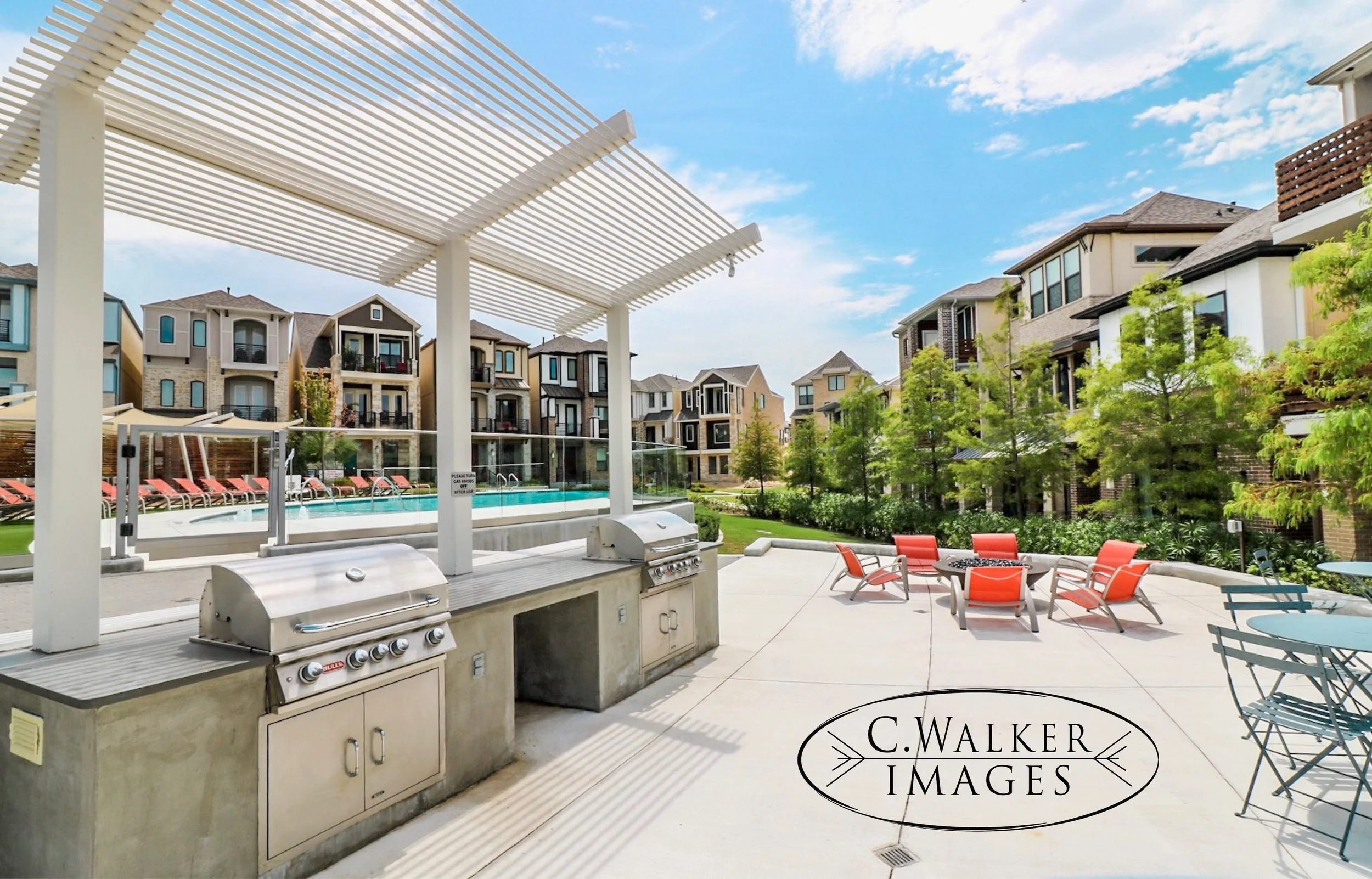 Outdoor communal area with grills, lounge chairs by a pool, and patio seating, surrounded by modern apartment buildings under a partly cloudy sky.