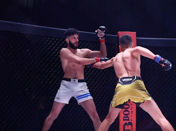 Mixed martial arts fight inside a cage, with one fighter delivering a punch to the other's face.