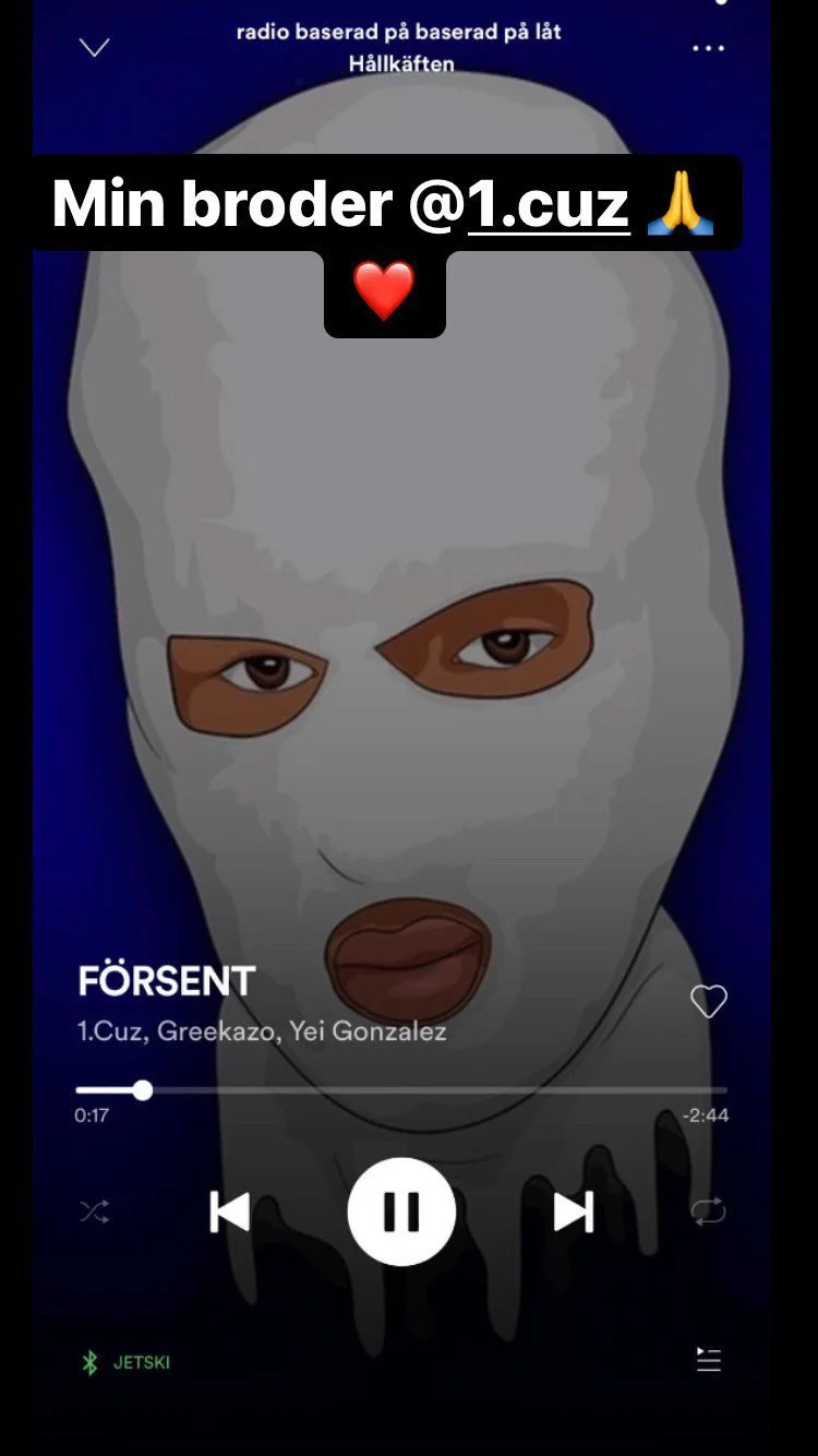 A person wearing a white ski mask covering the head, with eye holes and a mouth opening, visible on a music player screen showing the song "FÖRSENT" by 1.Cuz, Greekazo, Yei Gonzalez.