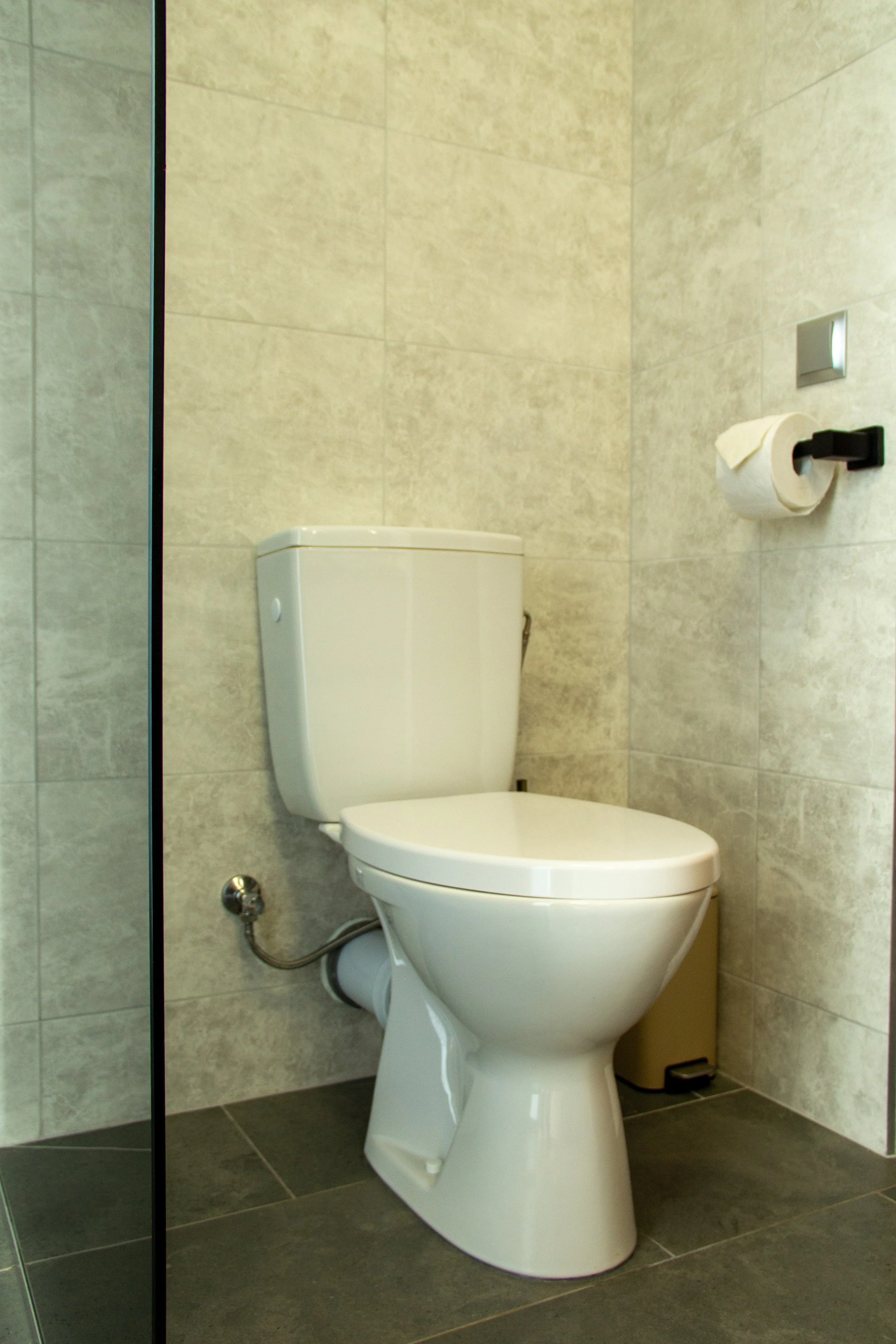 Toilet in a modern bathroom with beige tiled walls and gray floor.