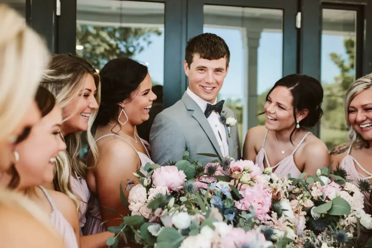 Groom-laughing-with-bridesmaids-soft-pink-dresses-sycamore-tree-wedding.webp