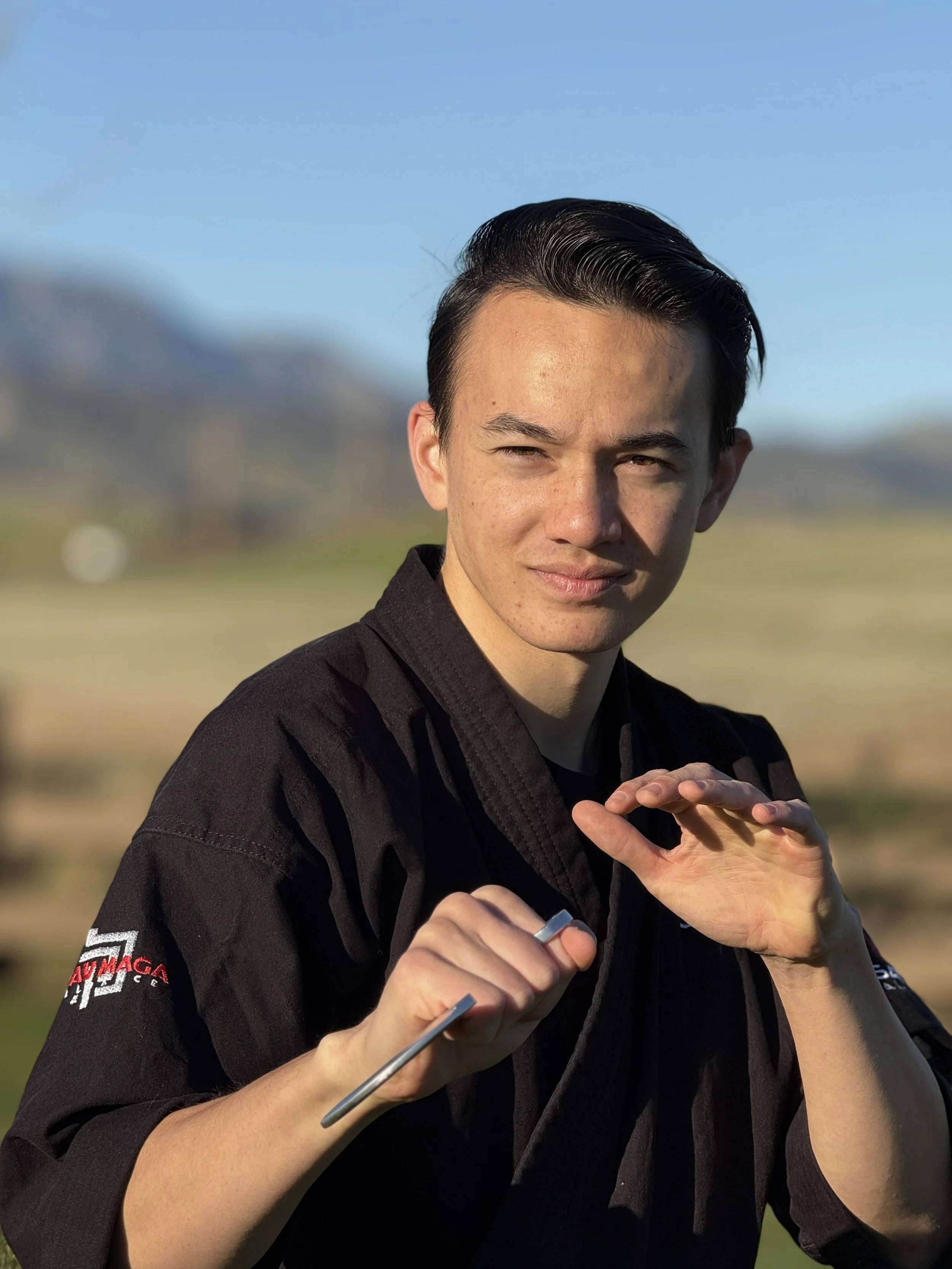 Young man in black martial arts uniform practicing martial arts outdoors.