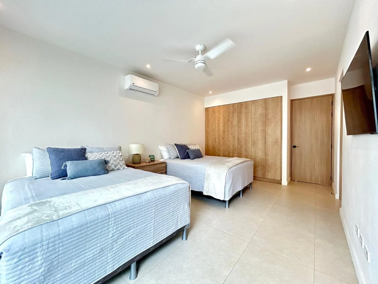 Habitación doble con camas, almohadas, mesita de noche, lámpara, aire acondicionado y televisión