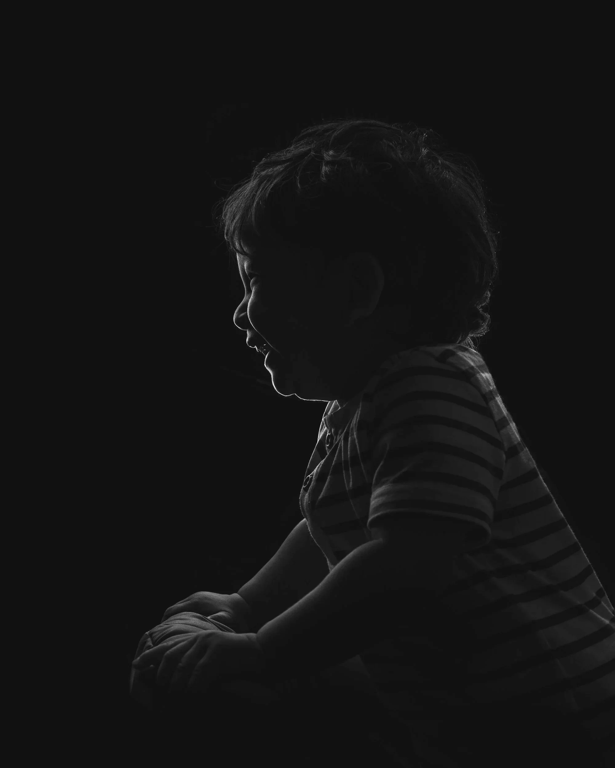 Silhouette of a smiling child with curly hair, wearing a striped shirt, against a dark background.
