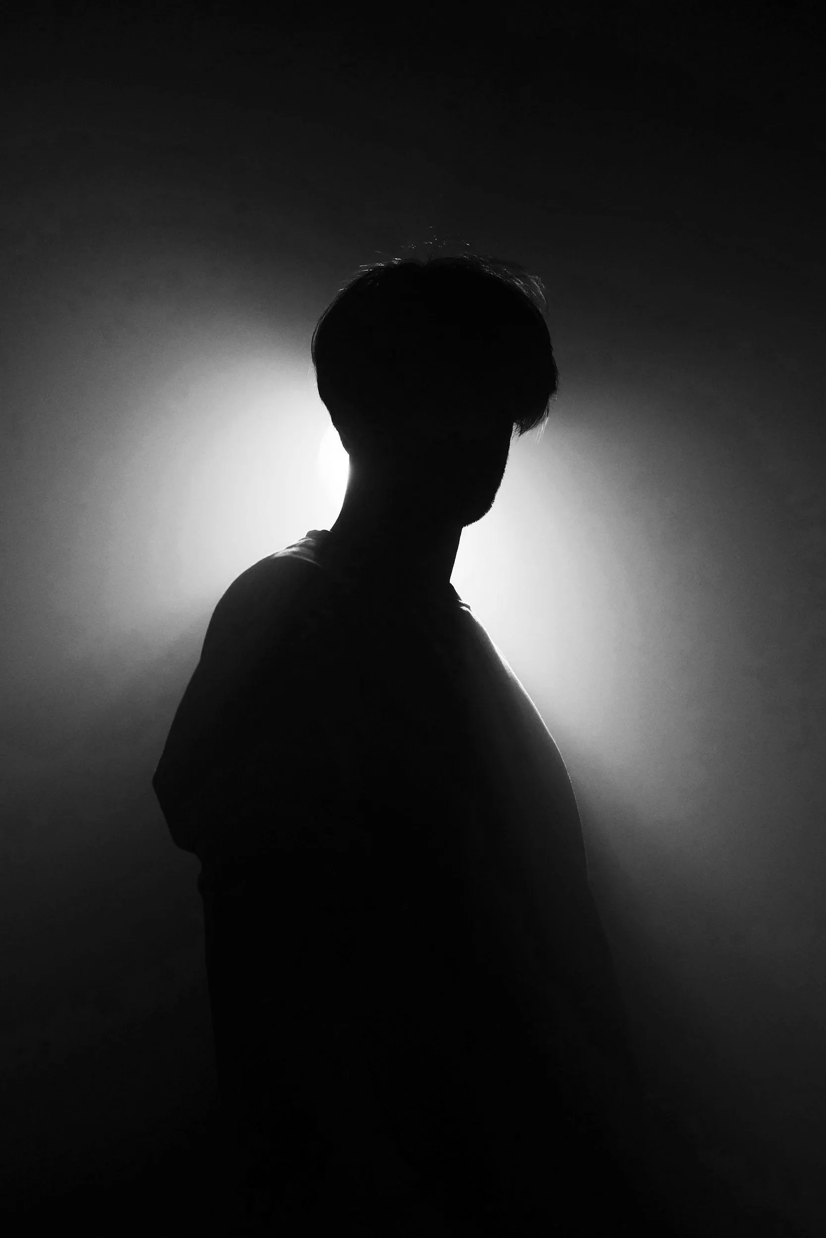 Silhouette of a person with short hair, turned to the side, against a bright light background, creating a dramatic shadow effect in black and white.