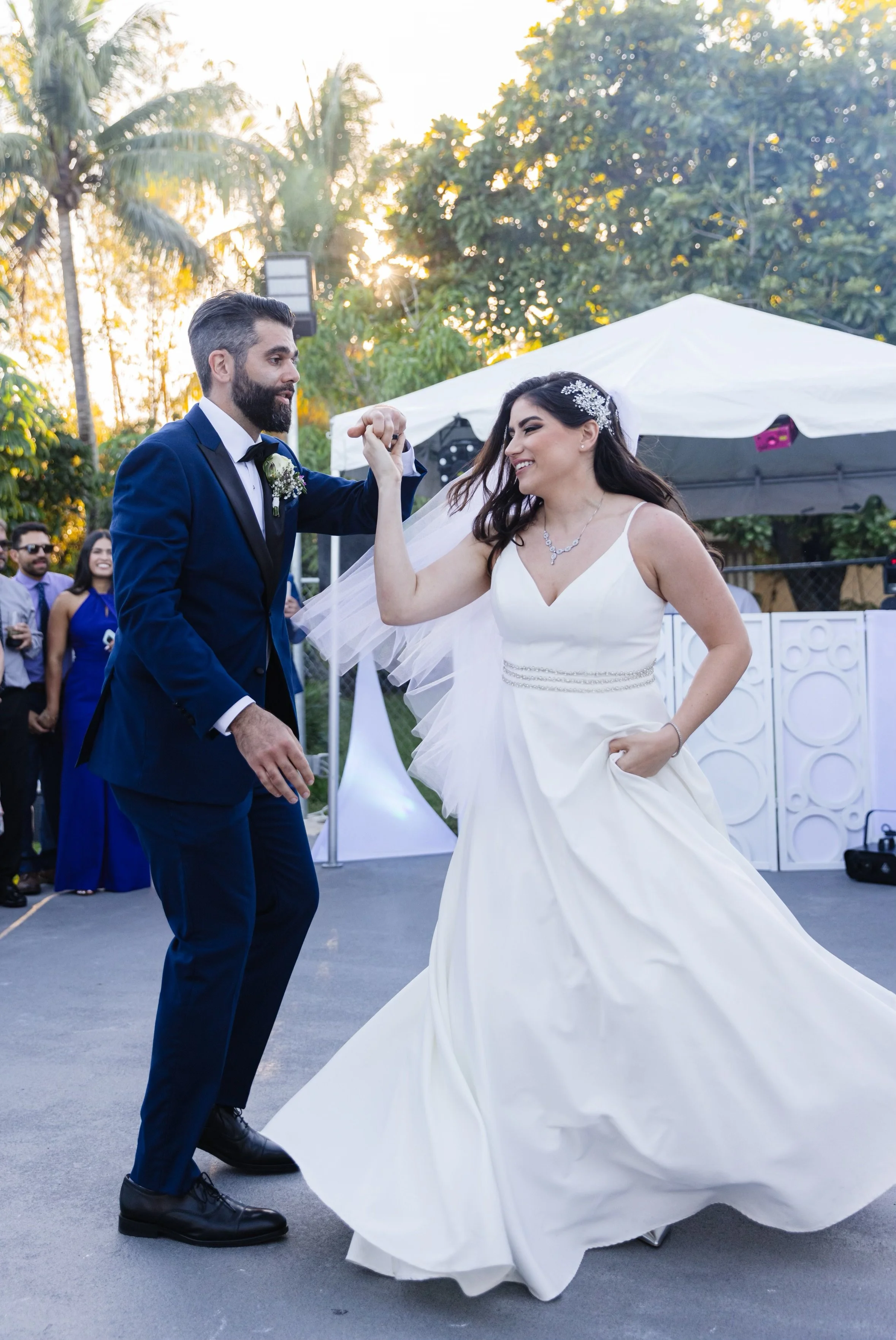 Bride and groom dancing at their wedding reception outdoors during sunset, with guests in the background.