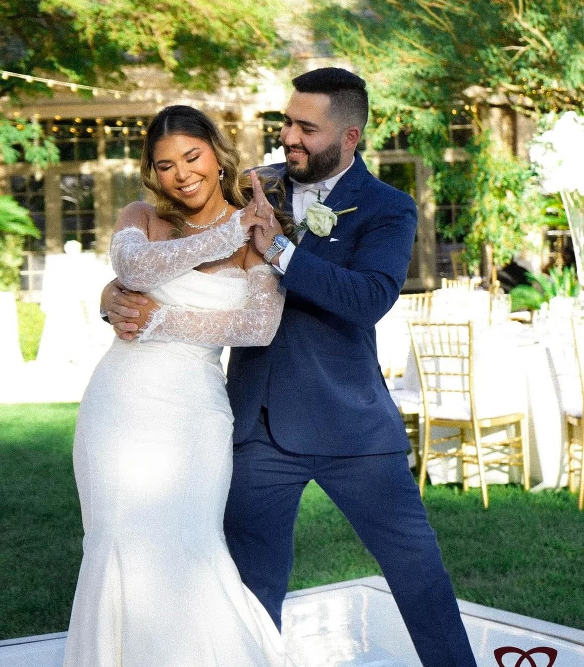 A newlywed couple dancing outdoors at their wedding reception, with tables and chairs in the background.