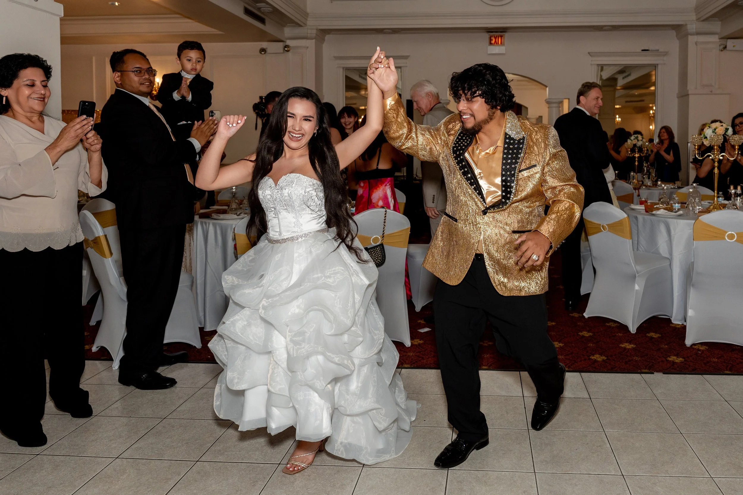 Bride and groom dancing at a wedding reception, with guests watching and taking photos in the background.