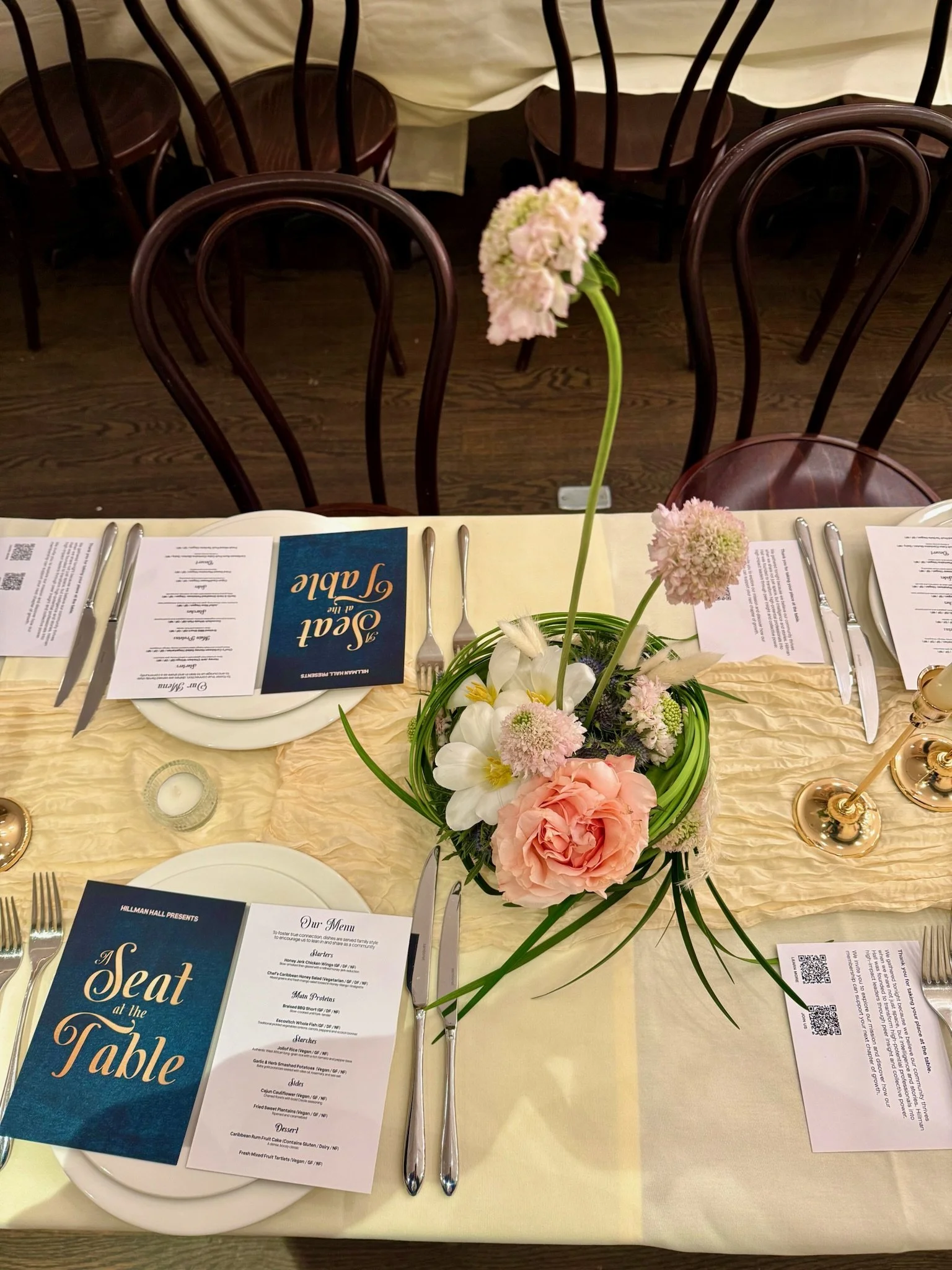 A decorated table set for a meal with a floral centerpiece, menus, and utensils in a restaurant or banquet setting.