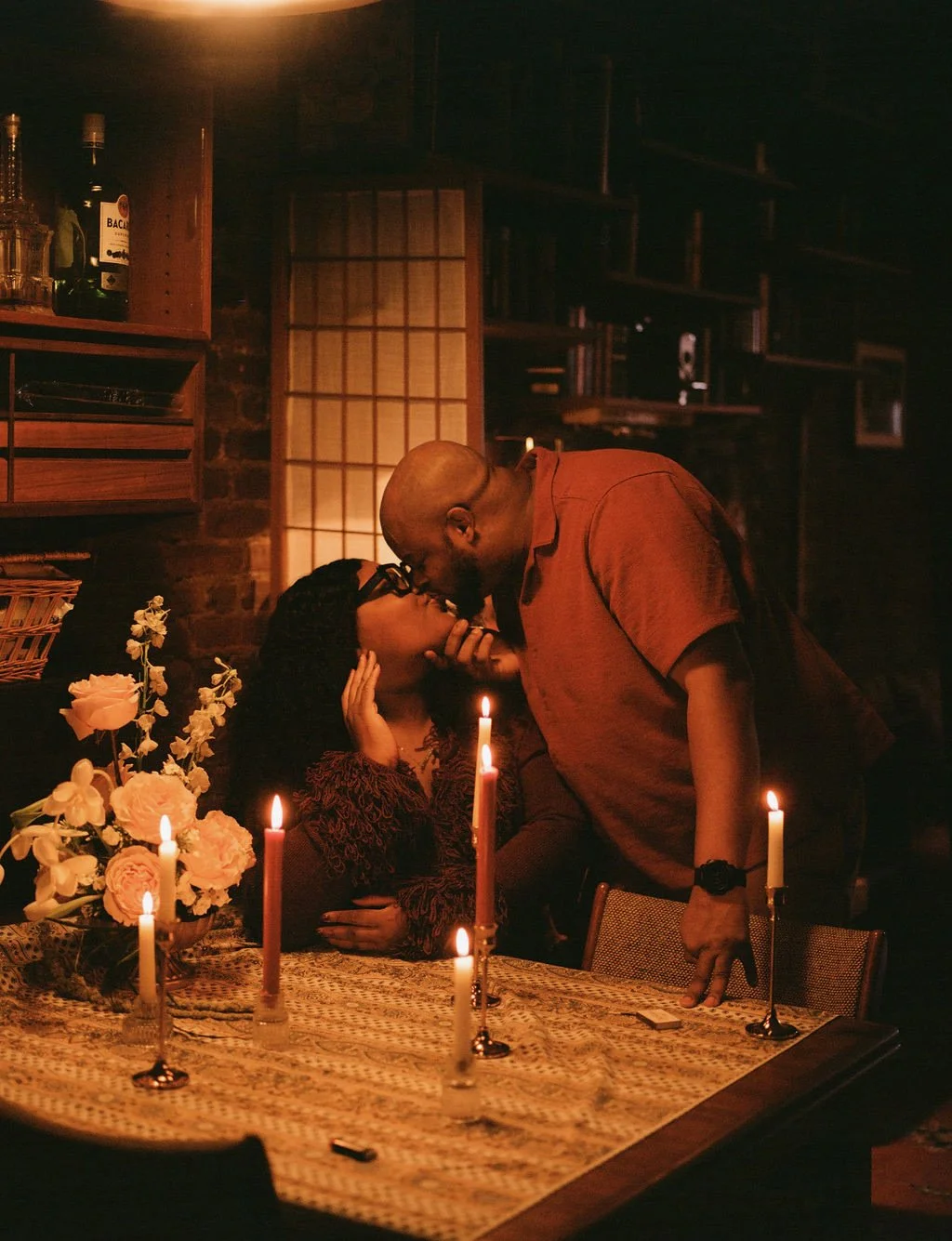 A couple sharing a romantic moment at a candlelit dinner, with candles and flowers on the table.