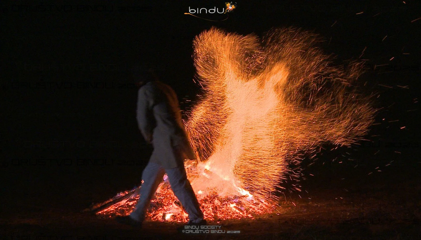 A person standing near a large burst of sparks from a firework or controlled firework explosion at night.