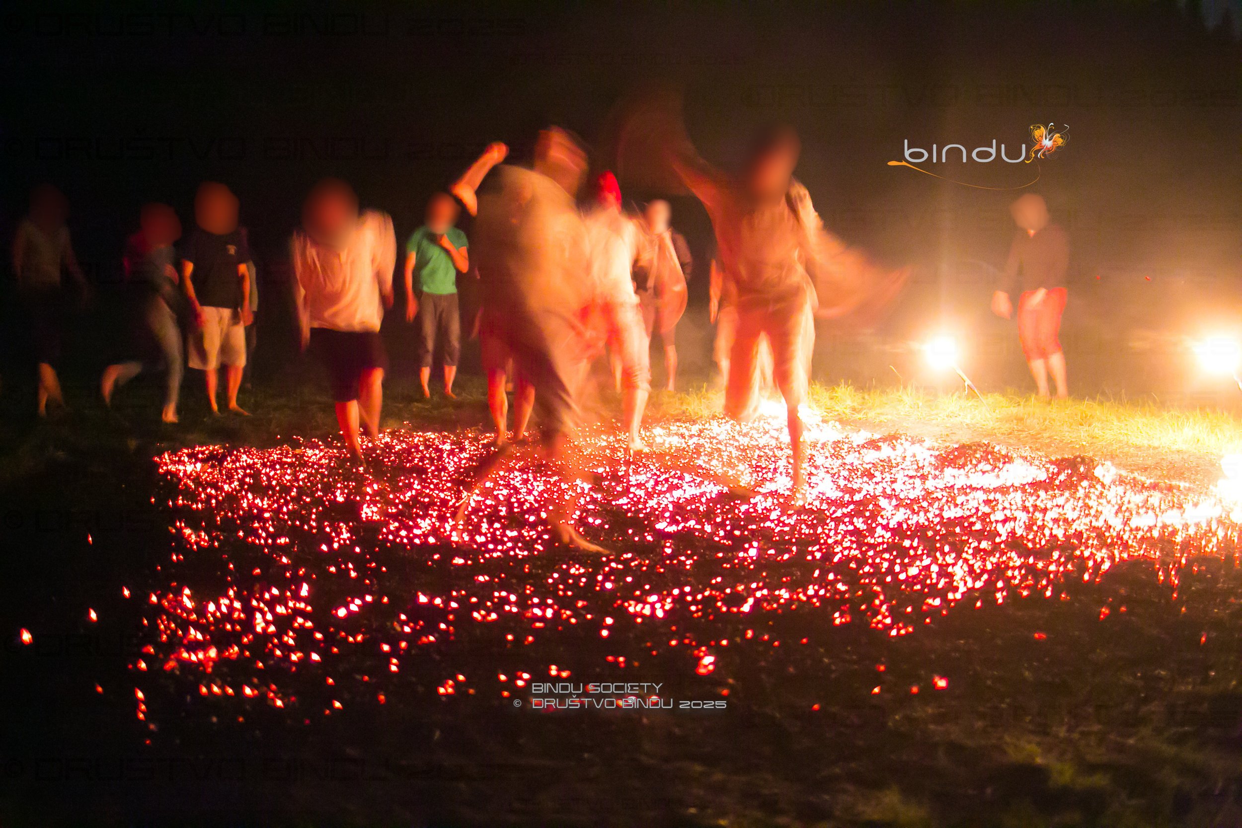 A group of people holding sparklers around a glowing fire on the ground at night.