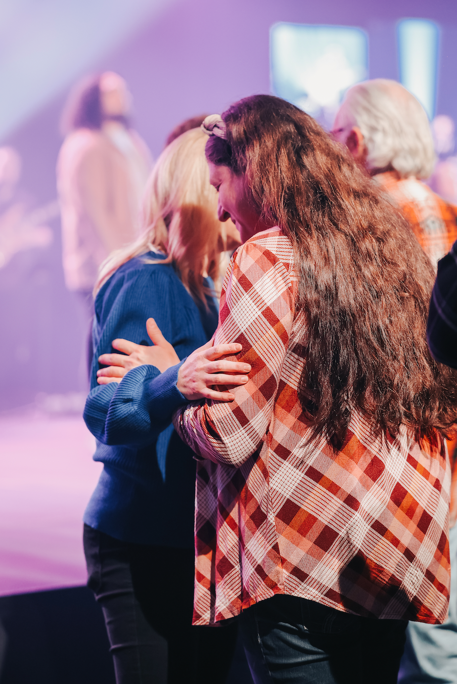People praying together with heads bowed and hands on each other's shoulders in a church or worship setting.