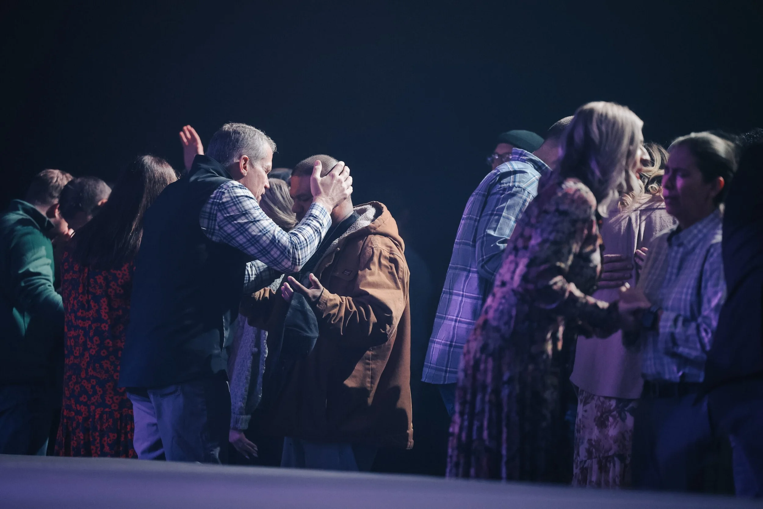 People praying and holding hands during a worship service on stage.