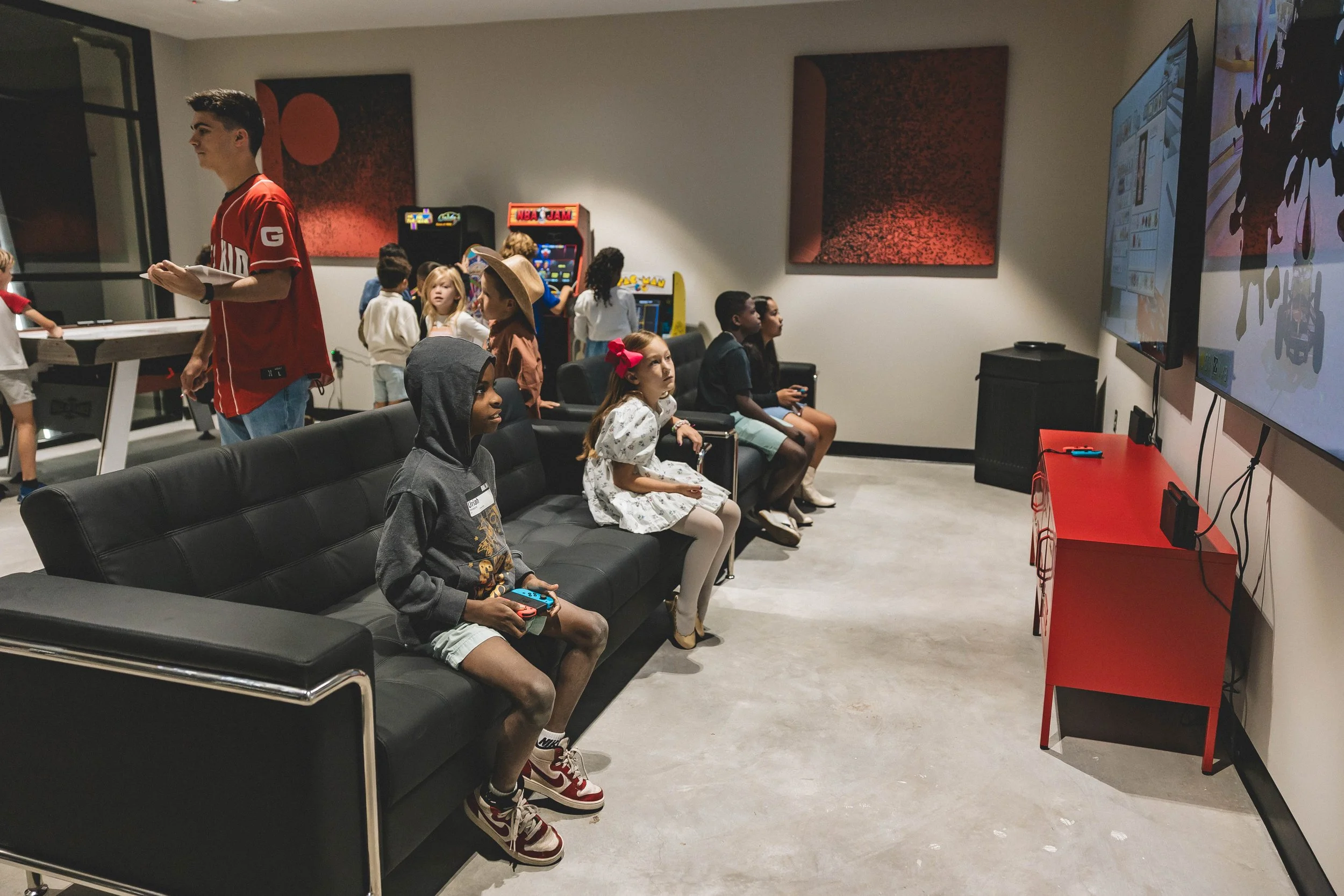 Kids playing video games and watching TV in a gaming lounge.