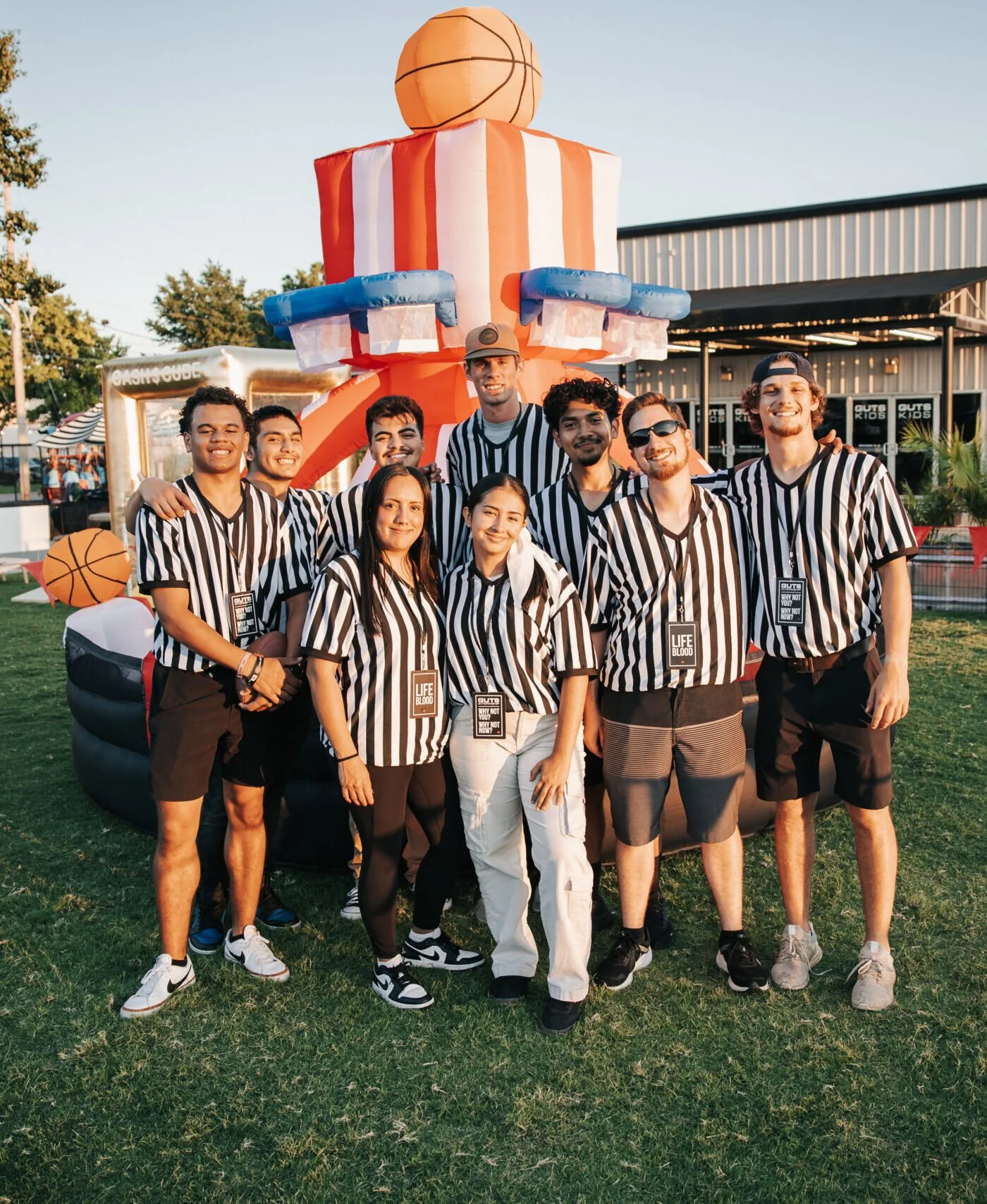 Group of young people in striped referee shirts posing in front of inflatable basketball game at outdoor event