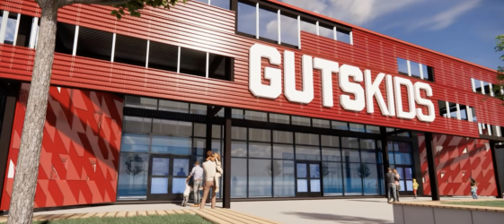 Exterior view of a modern building with a large sign reading GUTSKIDS, with people entering and standing outside.