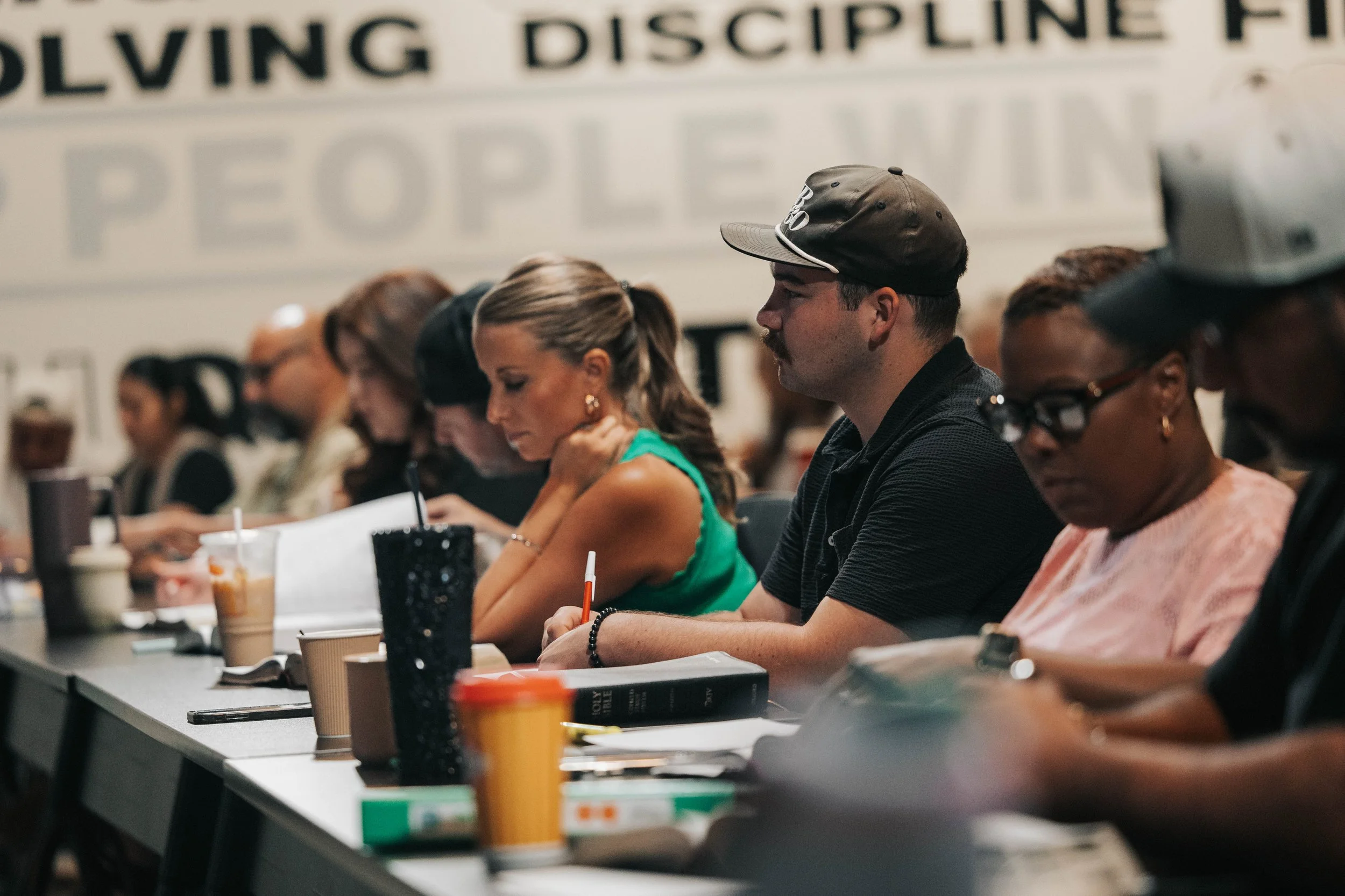 People sitting at a long table in a conference or seminar room, taking notes and listening attentively.