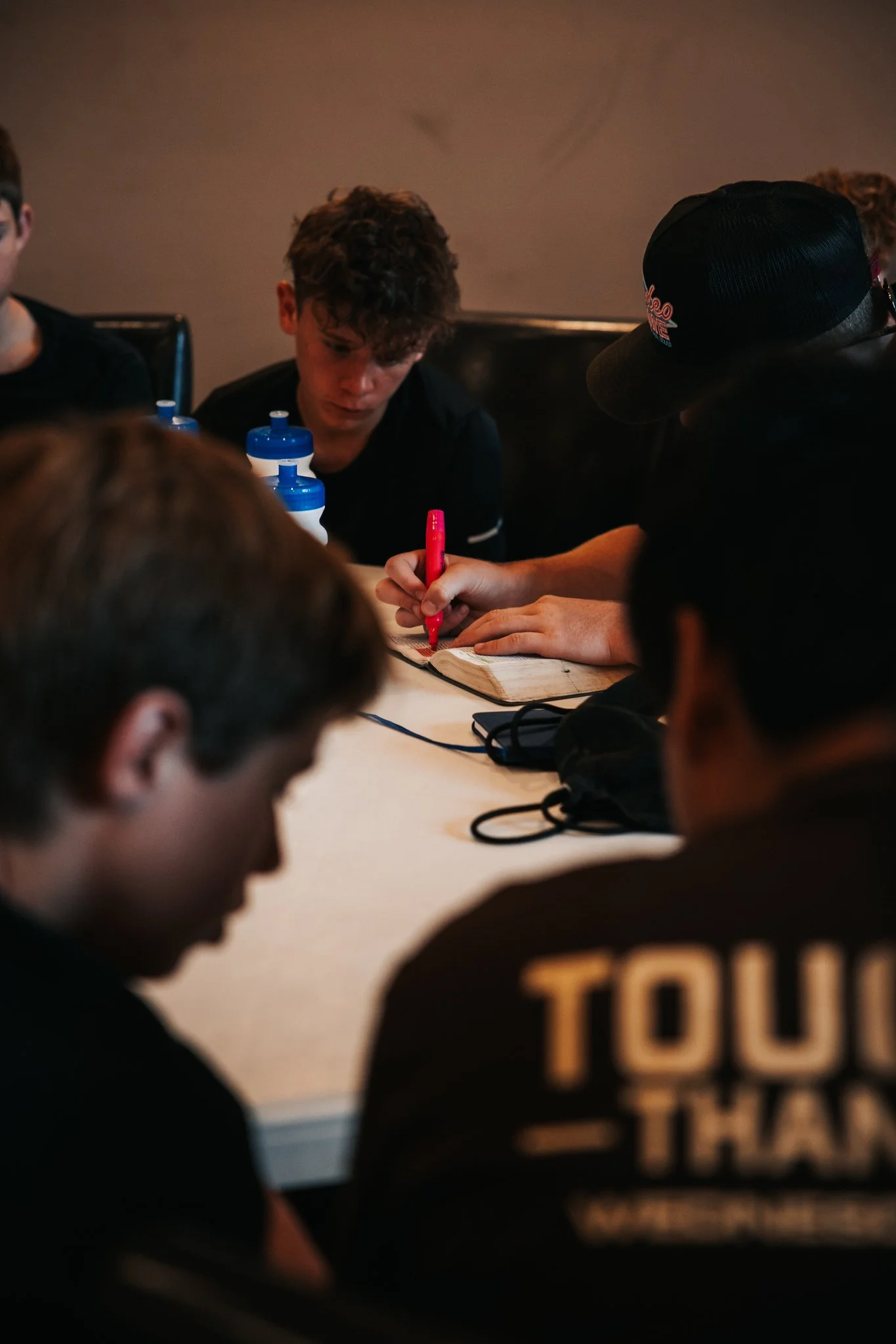 People gathered around a table, with some writing notes and others listening in a casual setting.