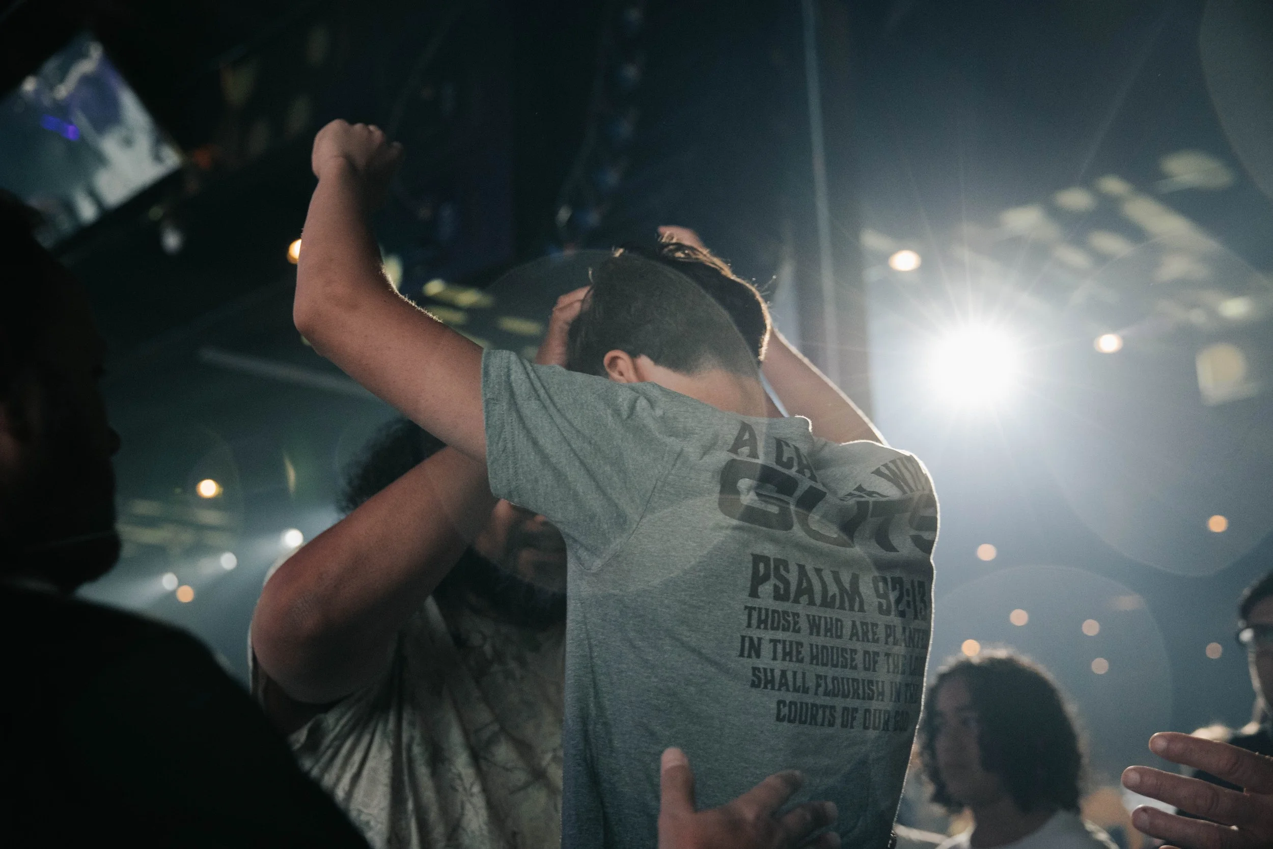 Two people embracing at a church event, with a bright light and people in the background.