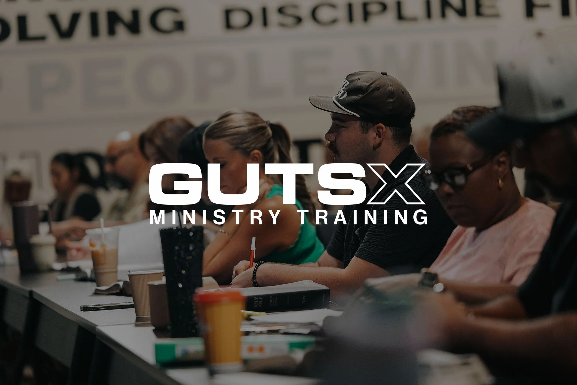 Group of people sitting at a long table during a ministry training event, with drinks and notebooks in front of them.