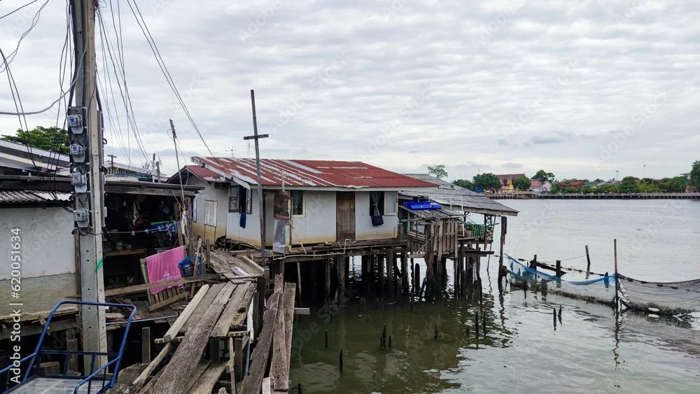 A stilt house built over water, with a rusty metal roof, wooden dock, and small boats nearby.