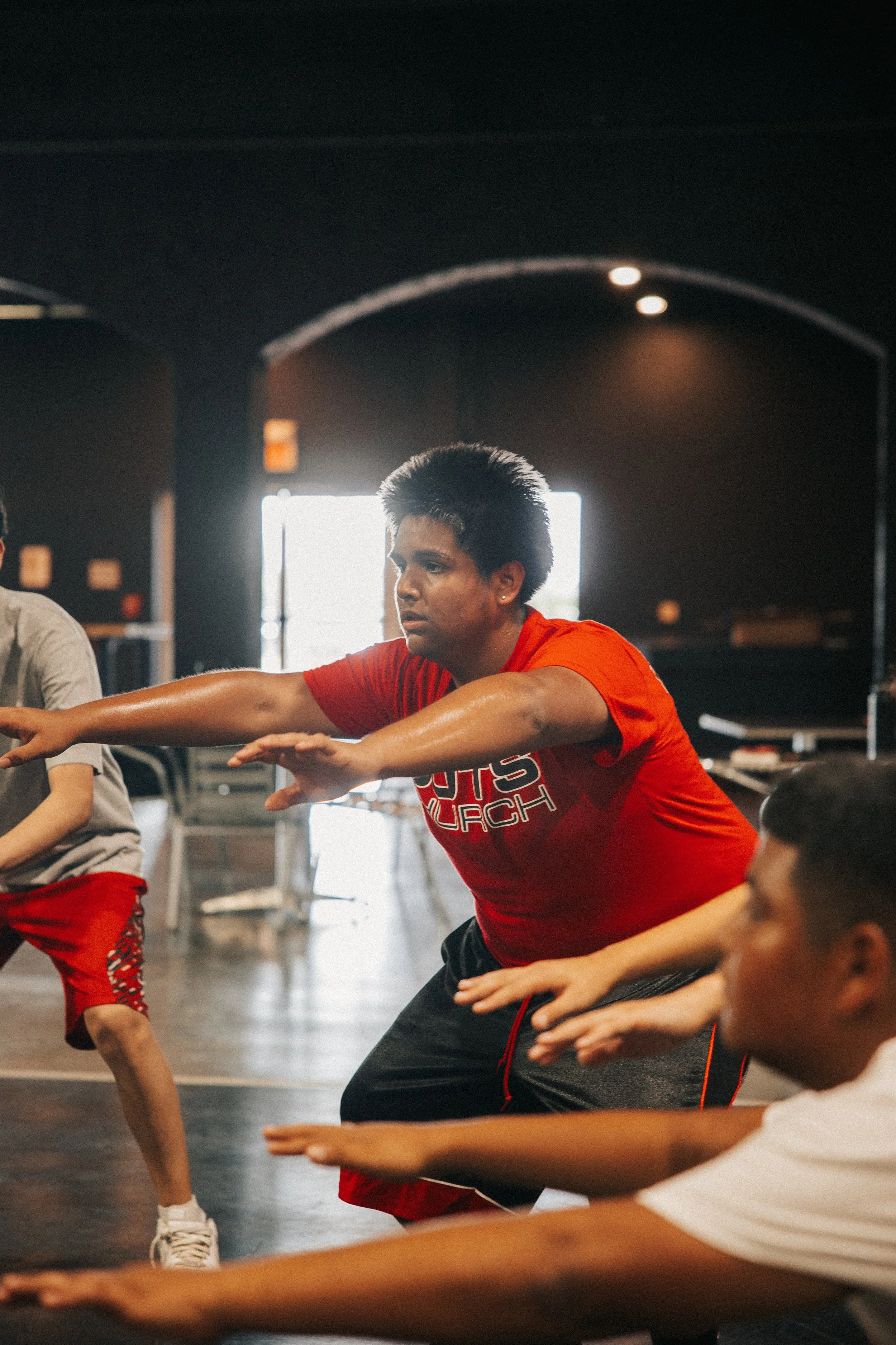 Young fitness instructor leading a workout class with children in a gym.
