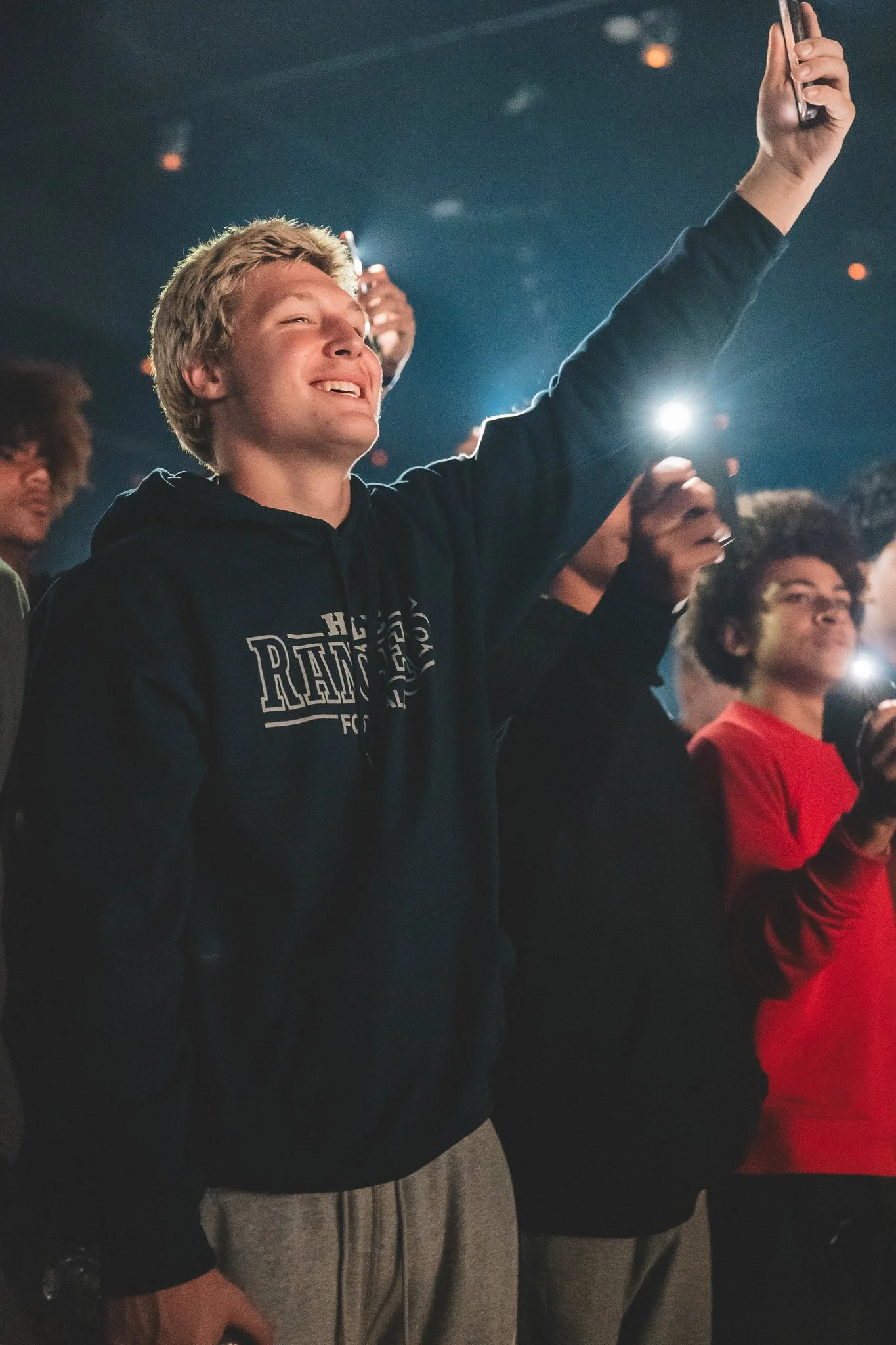 Young man taking a selfie at a concert or event, smiling with his eyes closed, surrounded by others.