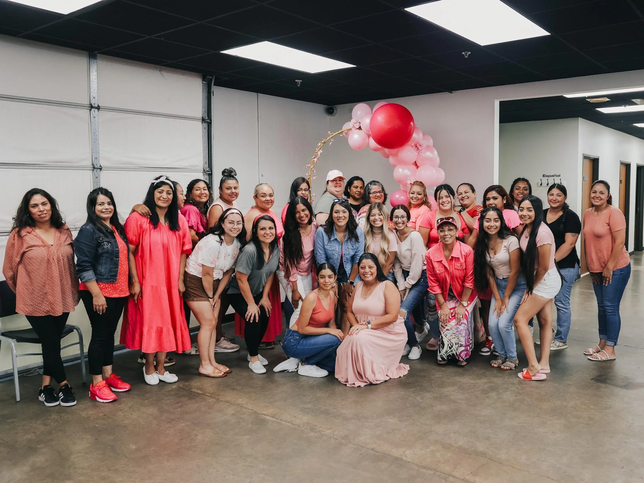Group of women gathered in a room decorated with pink balloons, smiling for a group photo.