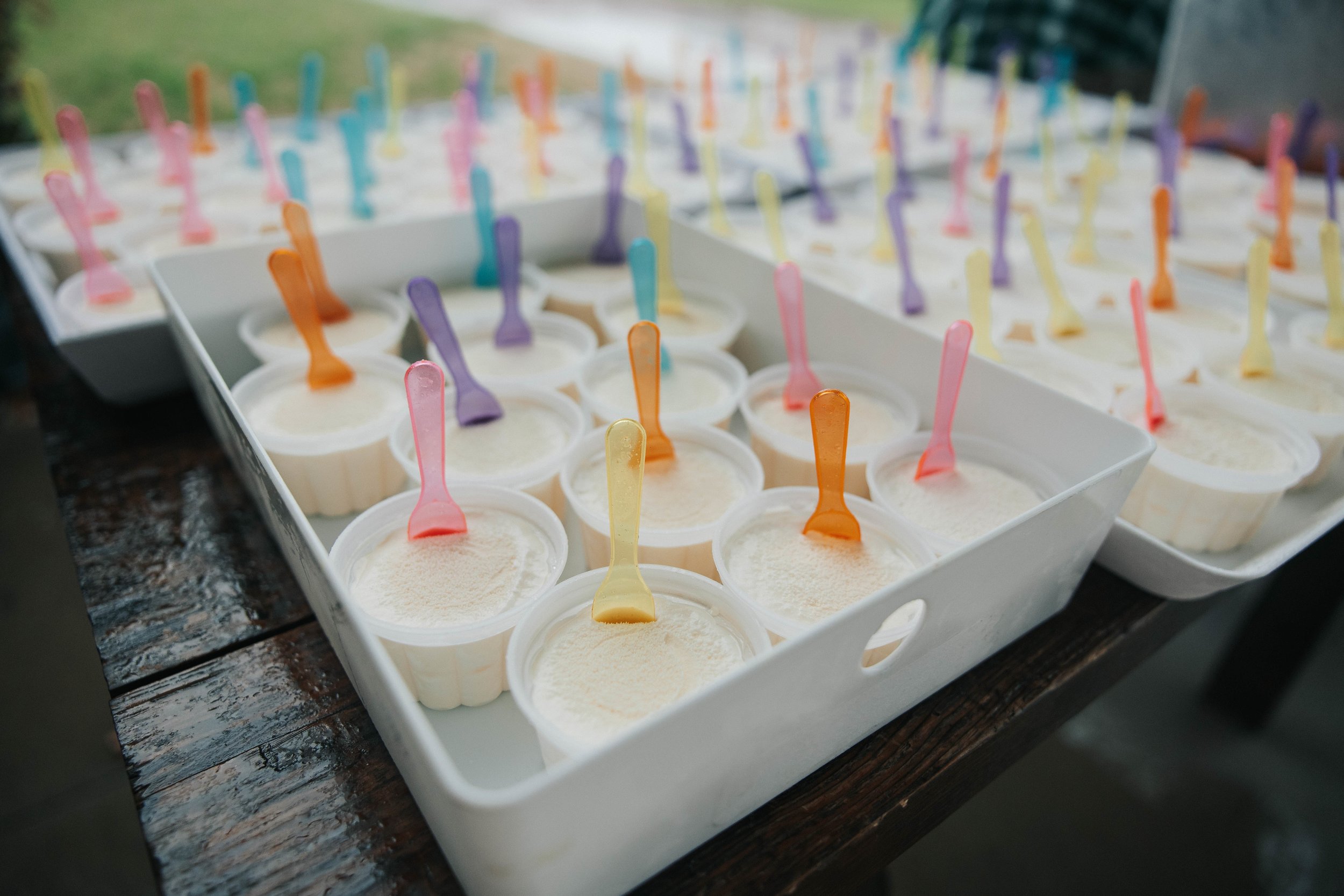 Several small cups of vanilla ice cream with colorful plastic spoons on a wooden table.