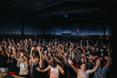 Crowd of people dancing and raising their hands at an indoor concert or event.