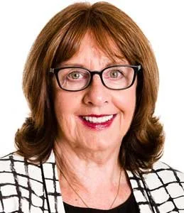 A woman with shoulder-length brown hair, glasses, and a checkered black and white blazer, smiling against a white background.