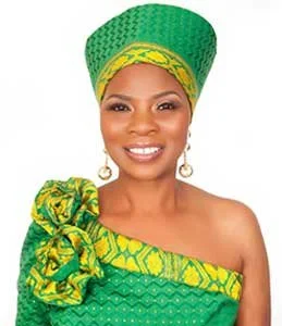 Portrait of a woman wearing traditional green and yellow attire with a matching headwrap, smiling.