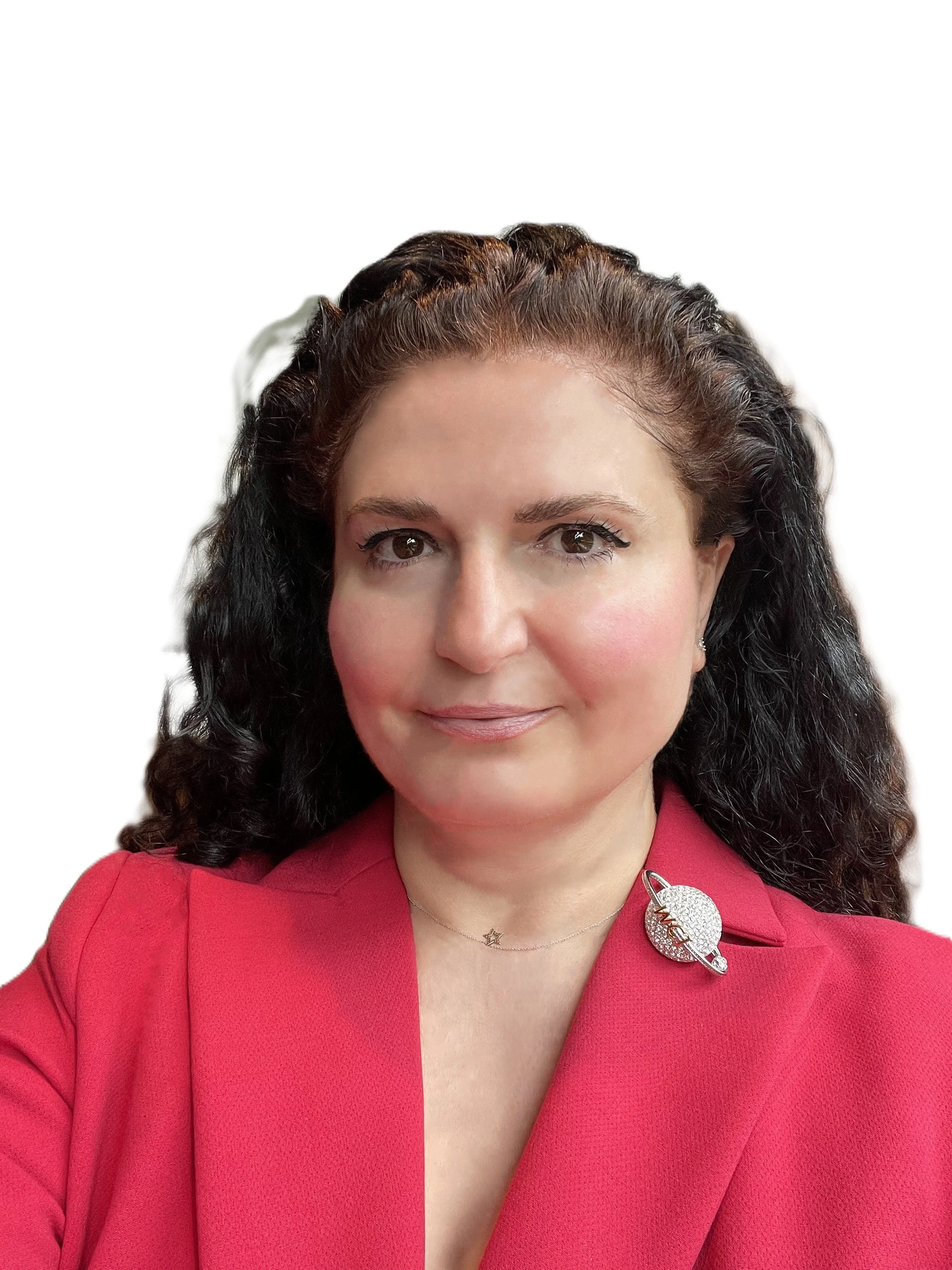 Portrait of a woman with dark curly hair wearing a red blazer with a planet-shaped brooch and a delicate necklace, against a plain white background.
