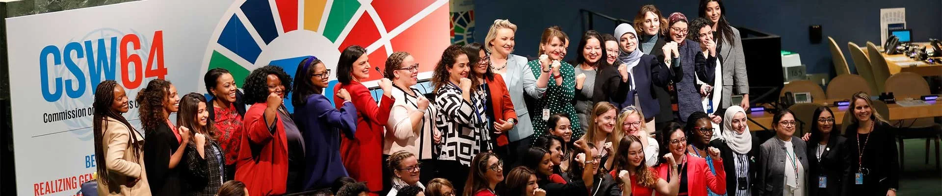 Group of women at a conference or event, posing for a group photo with a colorful banner in the background.