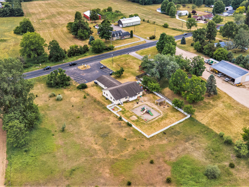Aerial view of Kid Star Daycare Center on Red Arrow Hwy in Paw Paw, Michigan, showing easy in/out driveway and large parking lot beside the fenced playground.