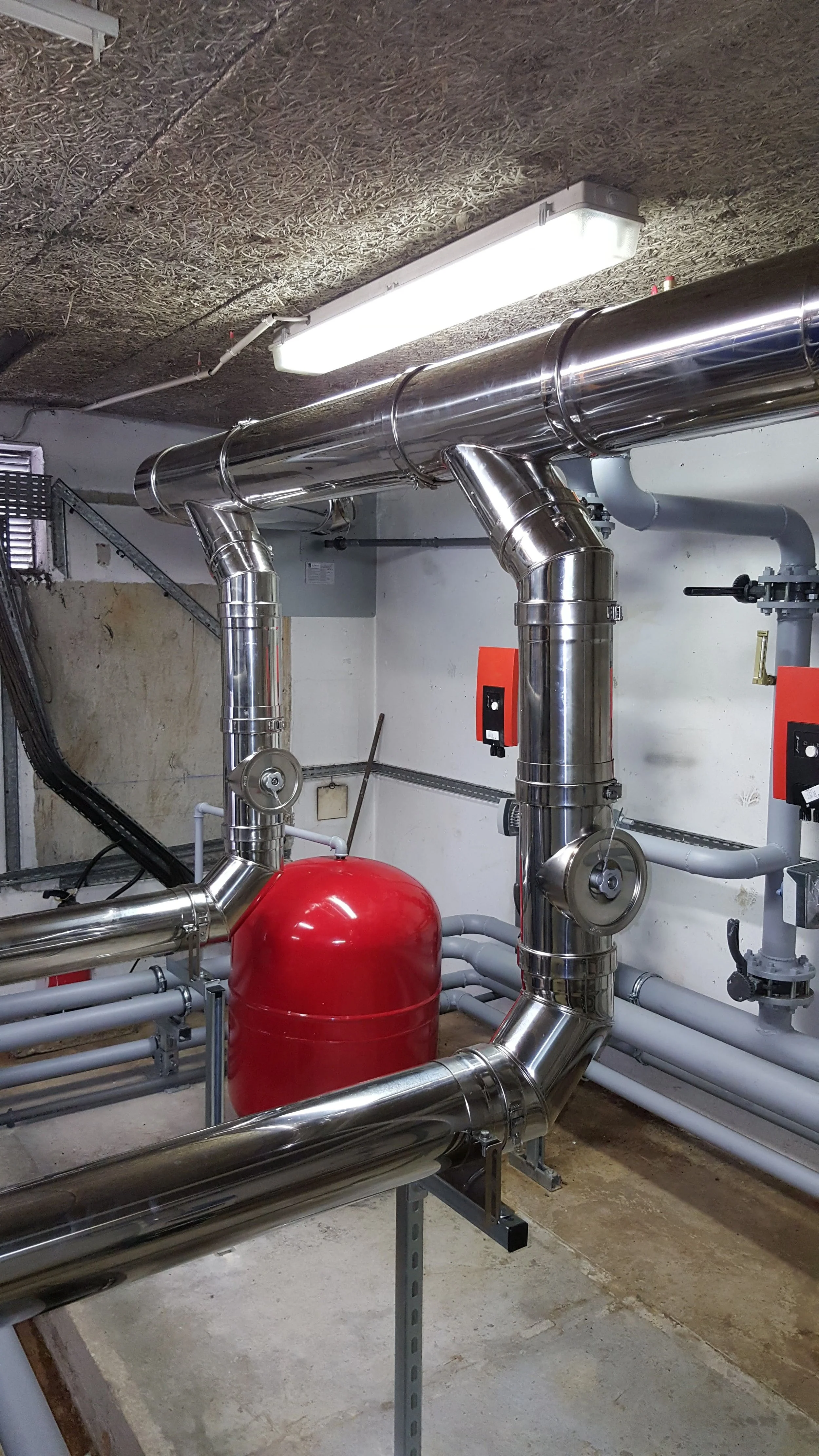 Un réseau de tuyaux en acier inoxydable avec une vanne et un réservoir rouge dans une salle de machine.