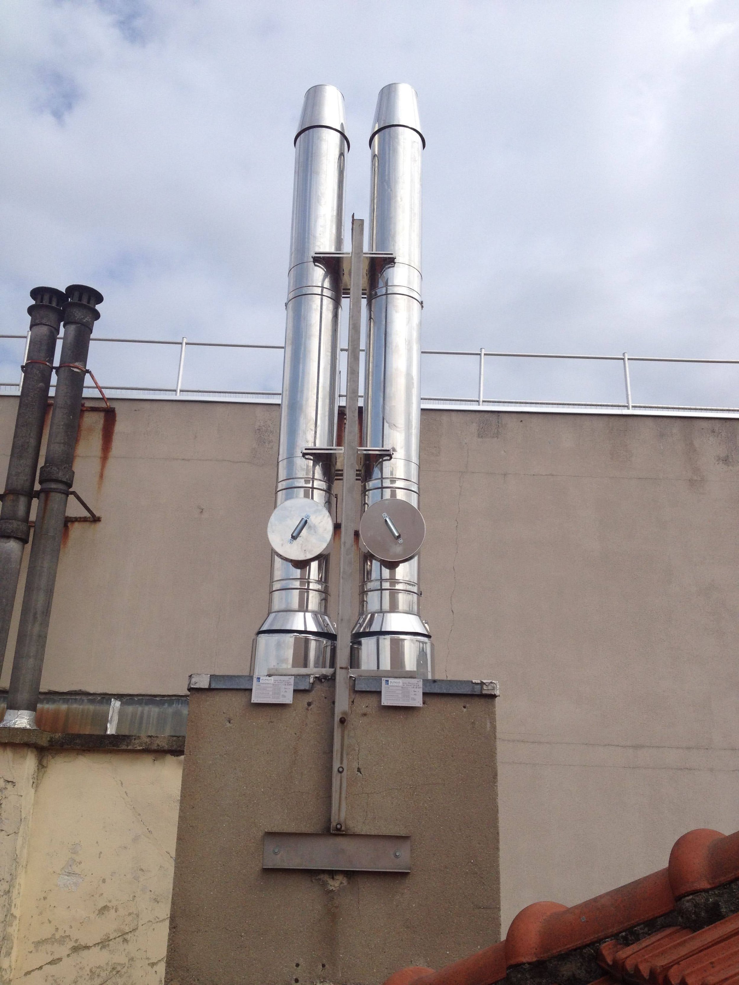 Deux grandes cheminées métalliques verticales sur un toit d'immeuble, avec un ciel nuageux en arrière-plan.