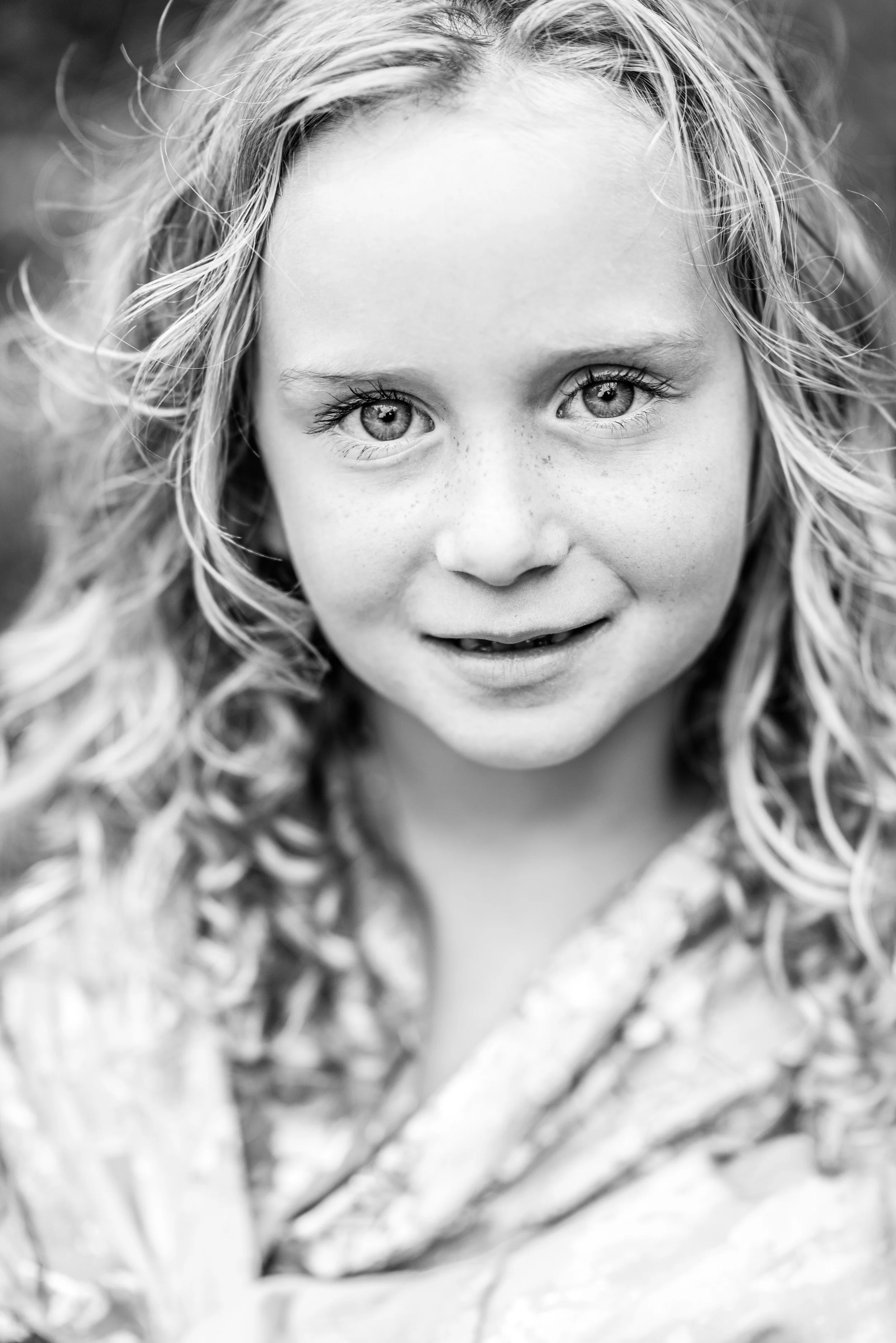 Close-up black-and-white portrait of a young girl with curly hair and freckles, smiling softly.