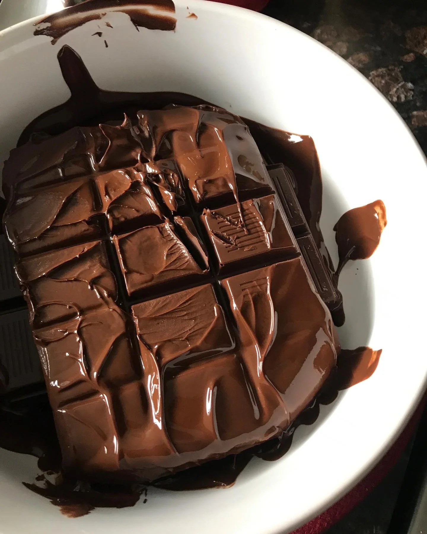 A bowl of melting chocolate, with some of it spilling over the side.