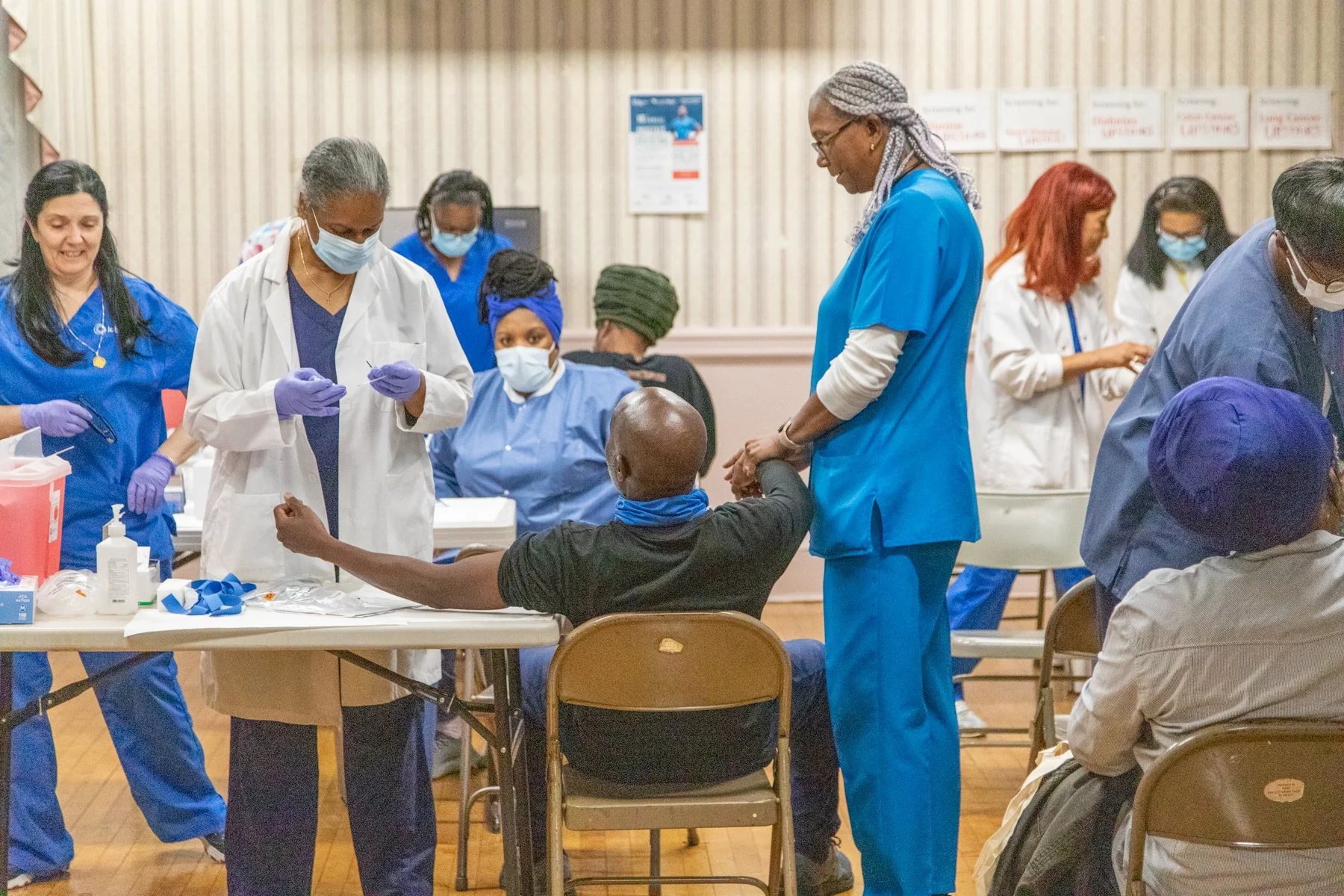 Medical staff and nurses in scrubs and masks working at a vaccination clinic, administering shots to patients and preparing medical supplies.